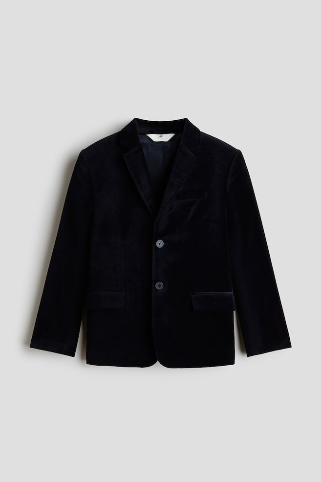 A dark velvet jacket is shown from the front, featuring notch lapels, a two-button front fastening, and a soft-textured finish. The structured design includes a welt chest pocket, two lower front flap pockets, and long sleeves. - 1