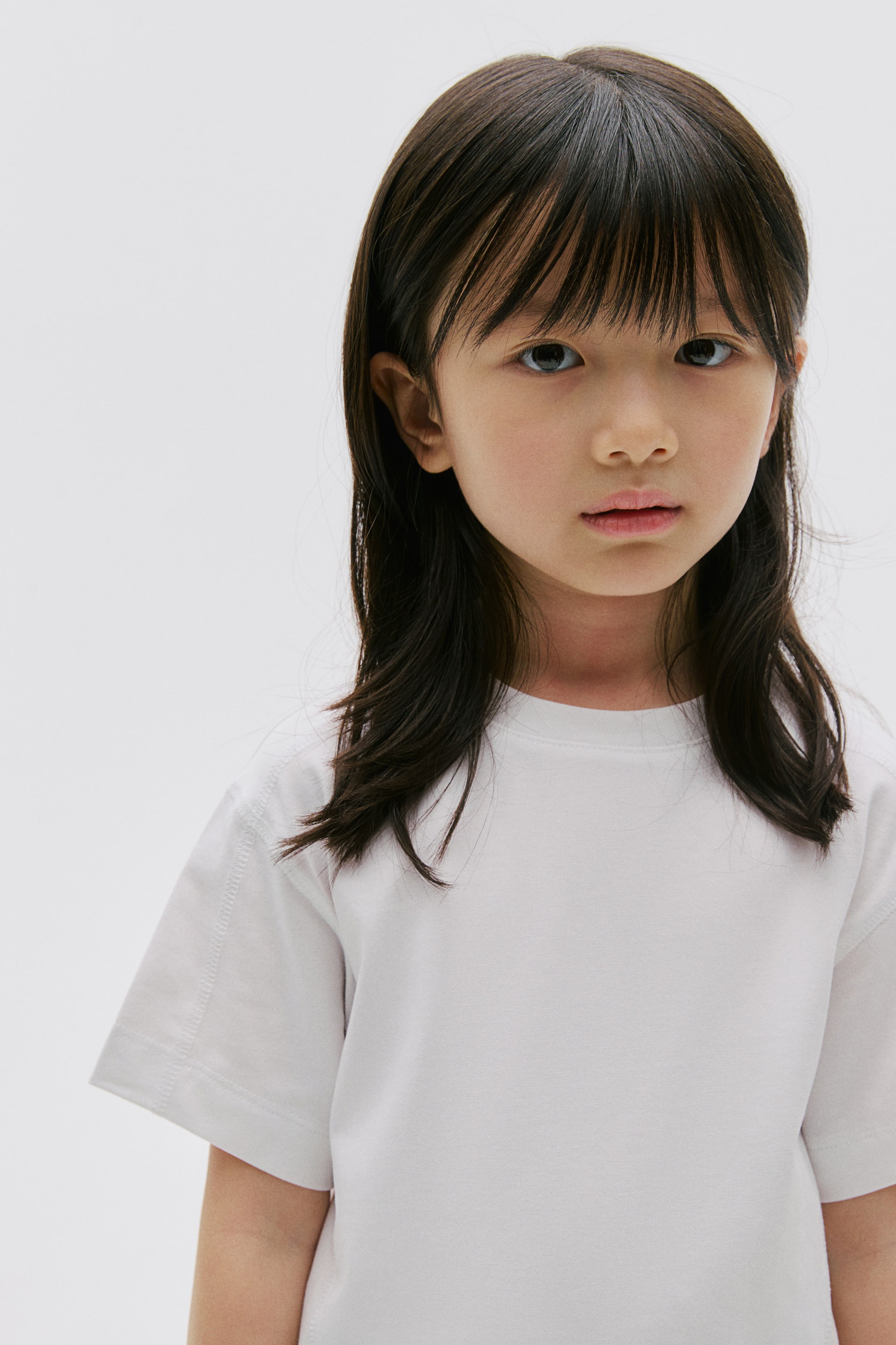 View larger image: A white crew neck t-shirt is featuring short sleeves with visible double-stitched seams along the shoulders and sleeve hems. It is displaying a smooth fabric texture and a relaxed fit.