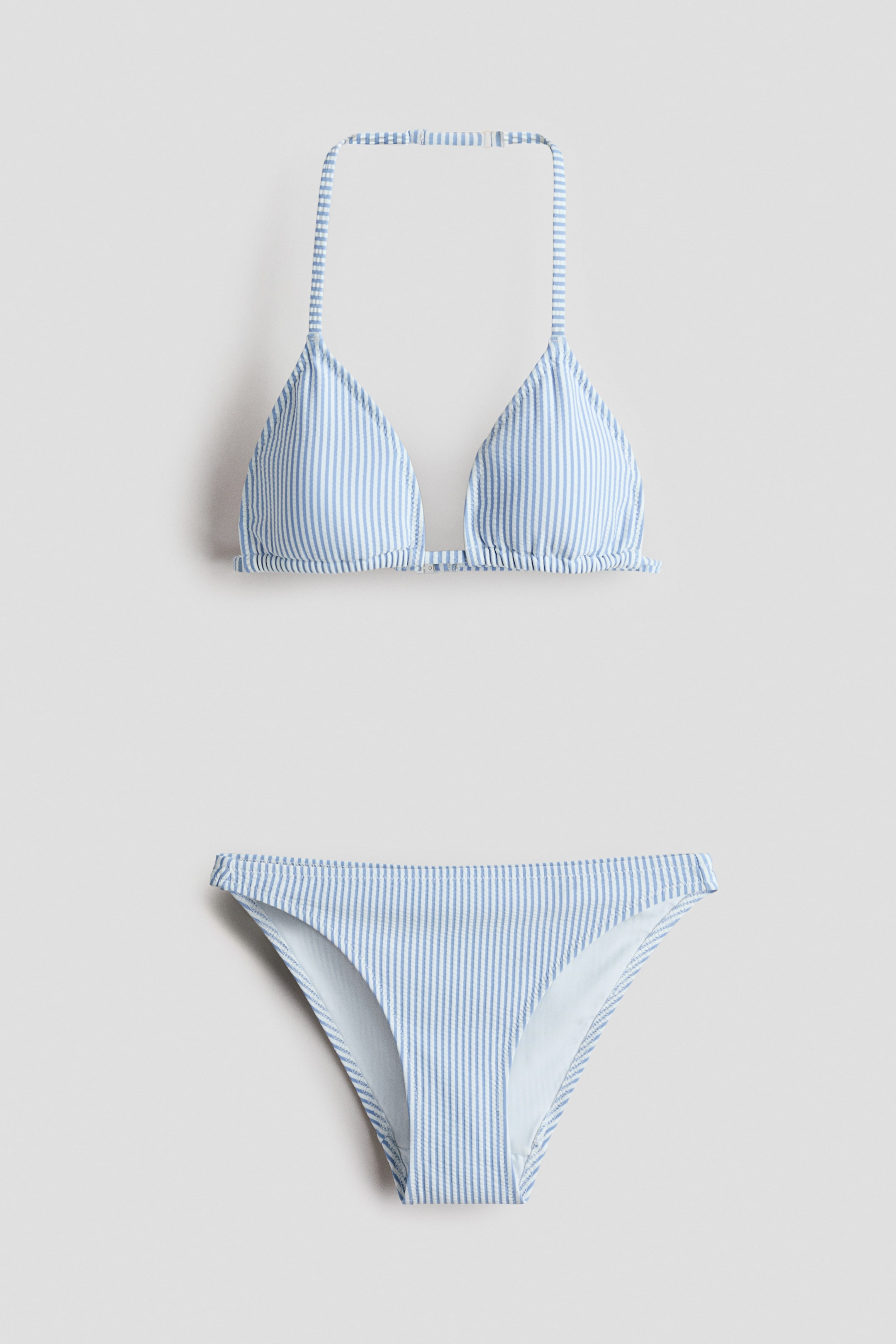 View larger image: A two-piece bikini set featuring a triangle top and matching bottoms, both adorned with light blue and white vertical stripes. The top is designed with an adjustable halterneck strap and a plastic fastener on its back strap.