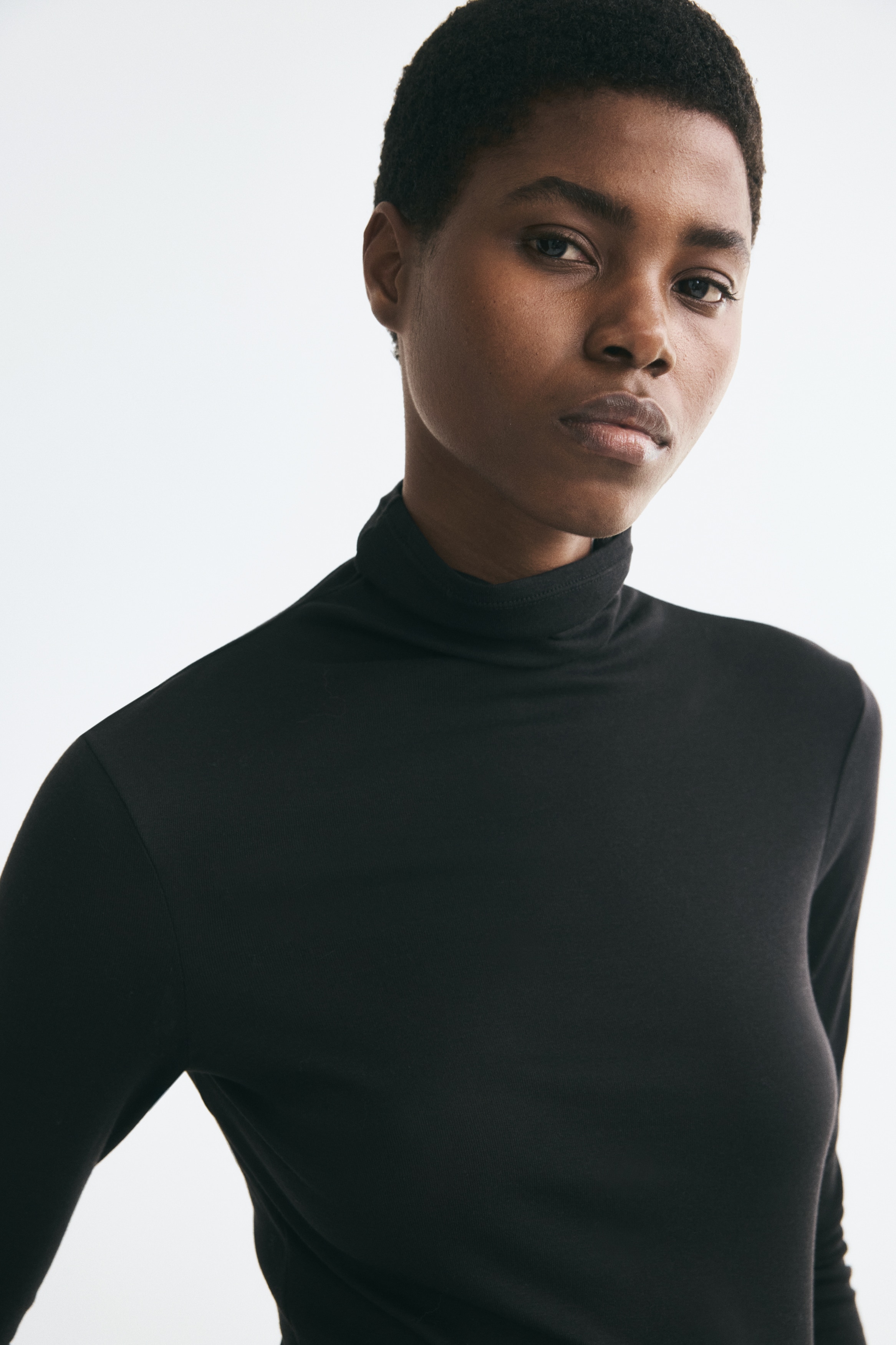 A black jersey top is being presented from the FRONT, featuring a rolled turtleneck and extra-long fitted sleeves.