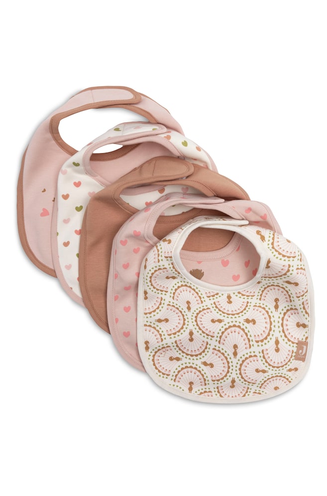 FÃ¼nf BabylÃ¤tzchen sind diagonal in einer Reihe Ã¼berlappend angeordnet und prÃ¤sentieren eine harmonisch abgestimmte Farbpalette aus zartem Rosa, Creme und Altrosa. Die LÃ¤tzchen zeigen verschiedene Designs, darunter einfarbige Varianten, verstreute Herzmuster und einen filigranen fÃ¤cherfÃ¶rmigen Grafikdruck auf dem vordersten LÃ¤tzchen, alle mit Klettverschluss am Halsausschnitt ausgestattet. - 1