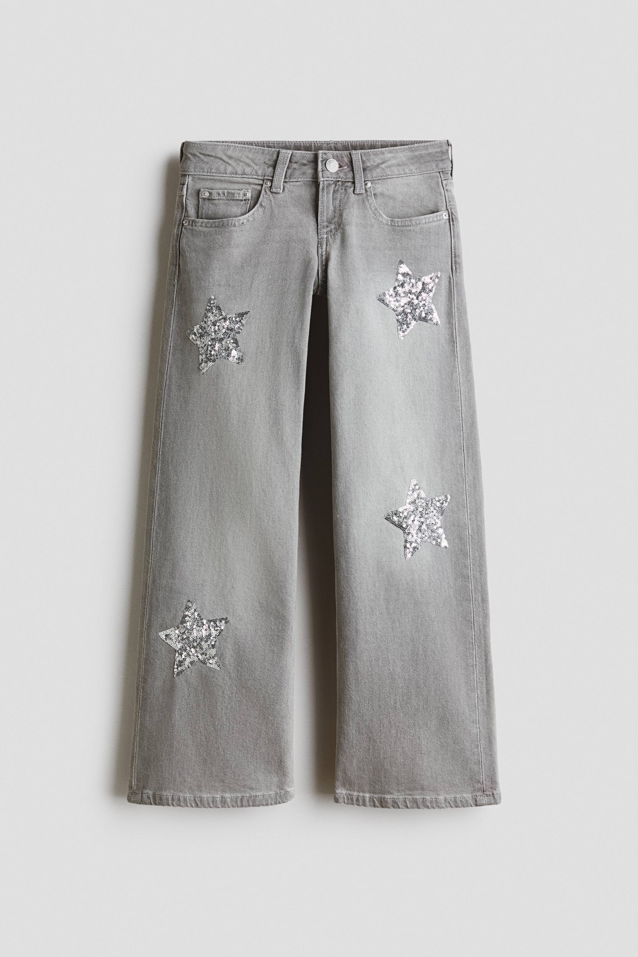 View larger image: Grey 5-pocket cotton denim jeans are showing a low waist, a button and zip fly fastening, and wide legs. Silver sequin stars are adorning the front of both trouser legs.