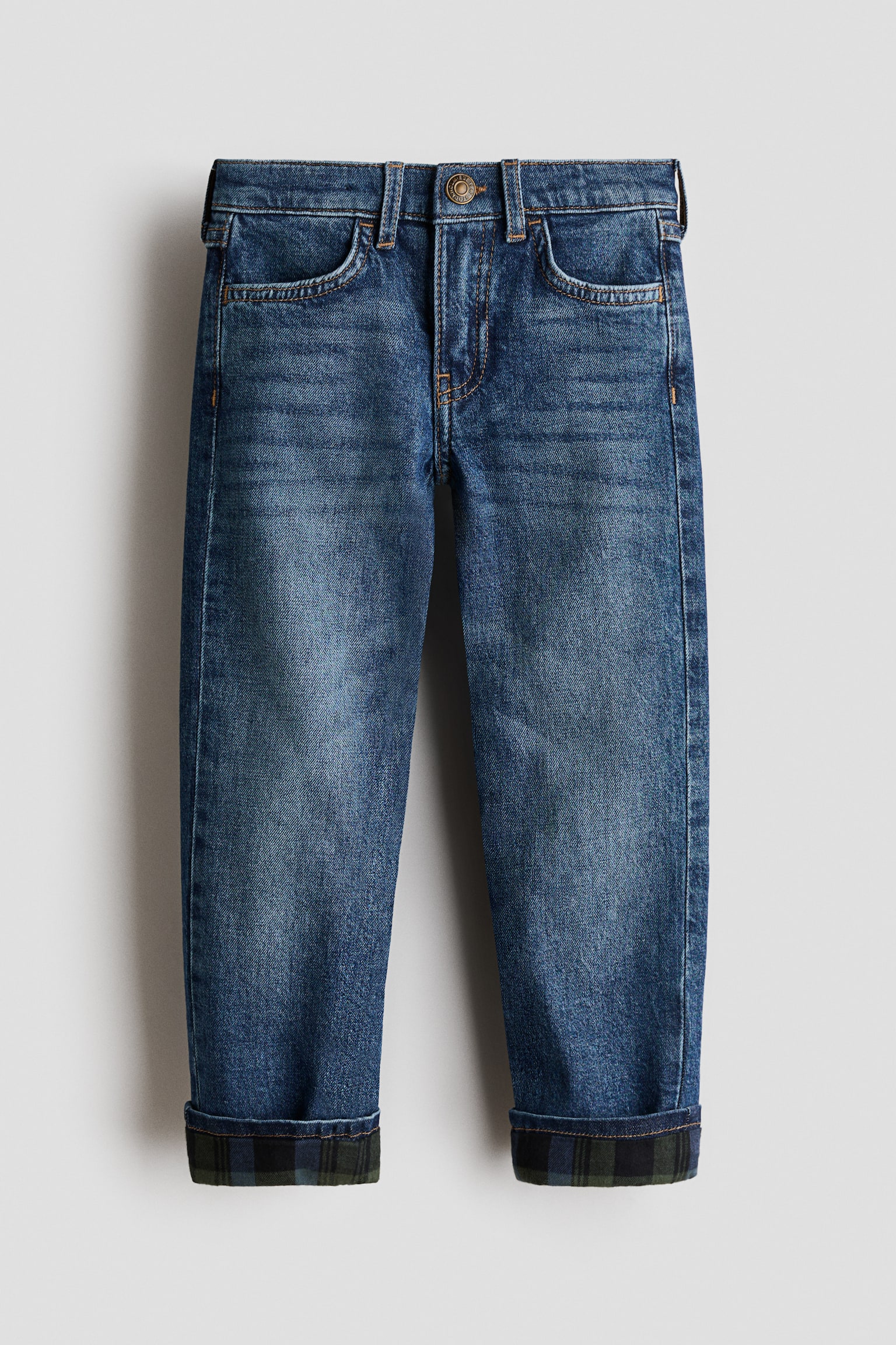 Ein Paar blau gewaschene Denim-Jeans ist von vorne zu sehen und verfügt über ein klassisches Five-Pocket-Design, Gürtelschlaufen und einen mittigen Knopfverschluss am Bund. Die Straight-Leg-Jeans haben umgeschlagene Beinabschlüsse, wodurch ein dunkelgrün-blau kariertes Stofffutter sichtbar wird.