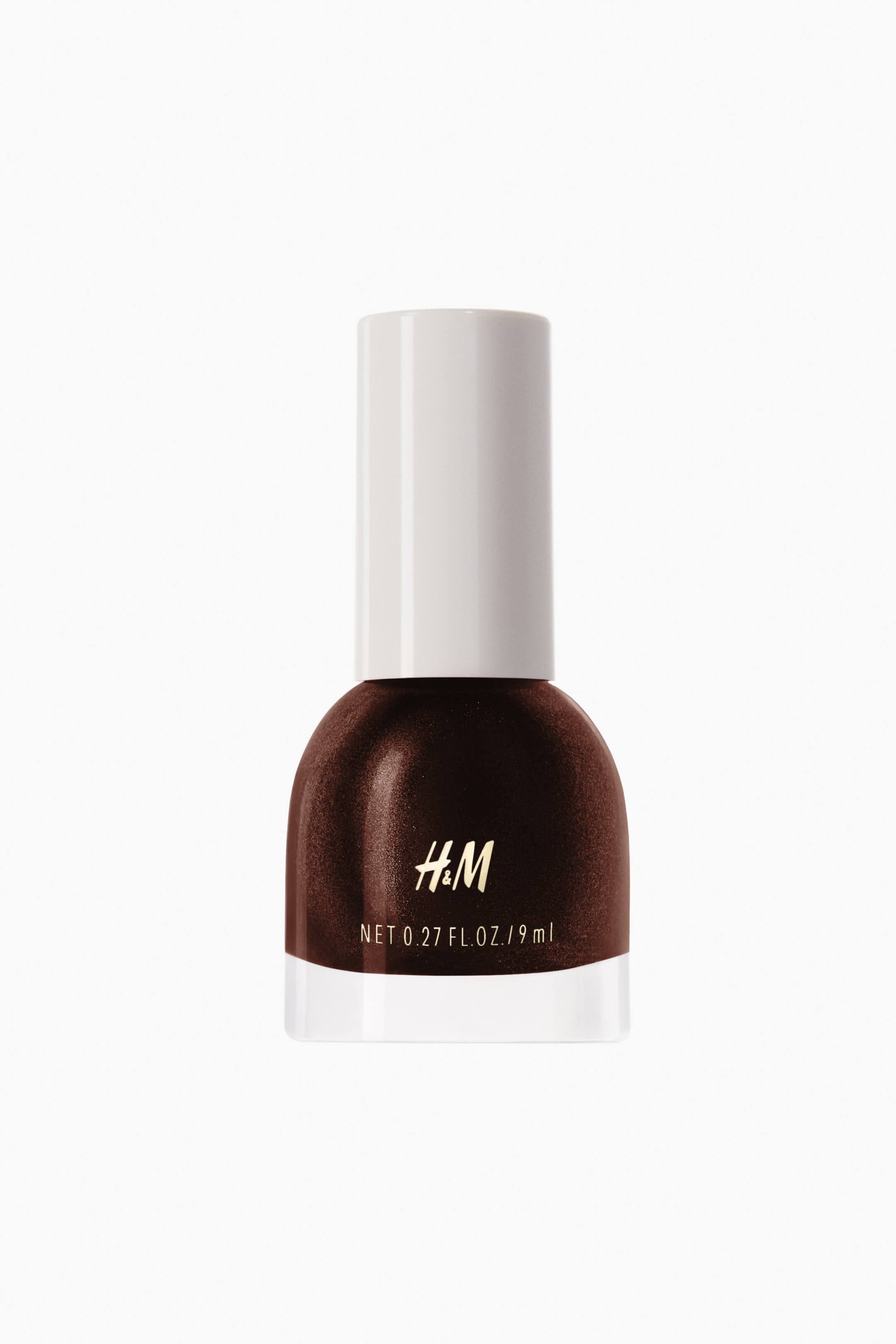 View larger image: The nail polish bottle, positioned facing forward, displays a rich shimmery brown shade. It features a white cylindrical cap and a transparent bottom section. The gold H&M logo and net volume details are prominently visible on the front.