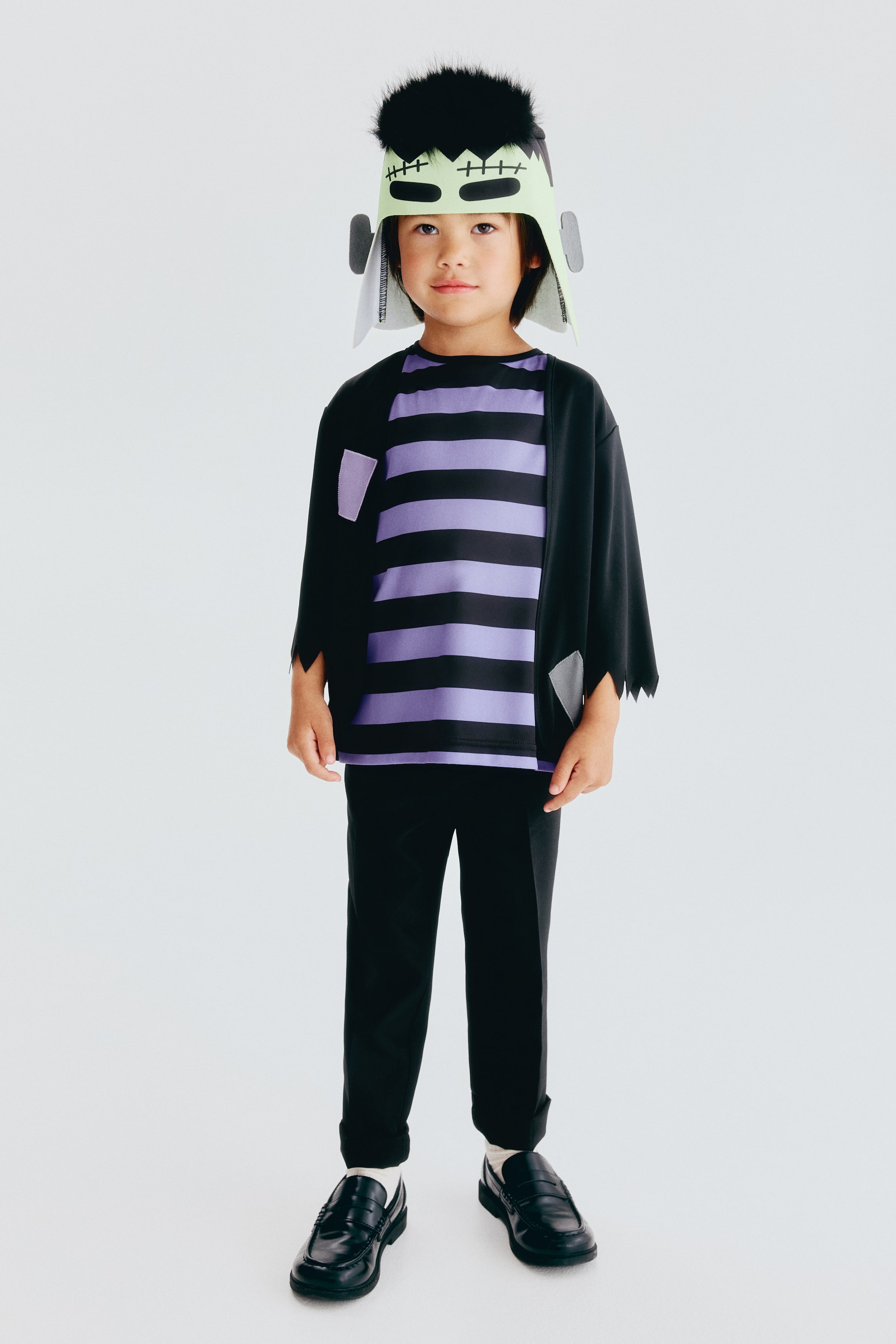 View larger image: A 2-piece monster costume set features a black, open-front outer top with jagged edges and grey patches, layered over a purple and black horizontal striped long-sleeve shirt. The set includes black straight-leg trousers.