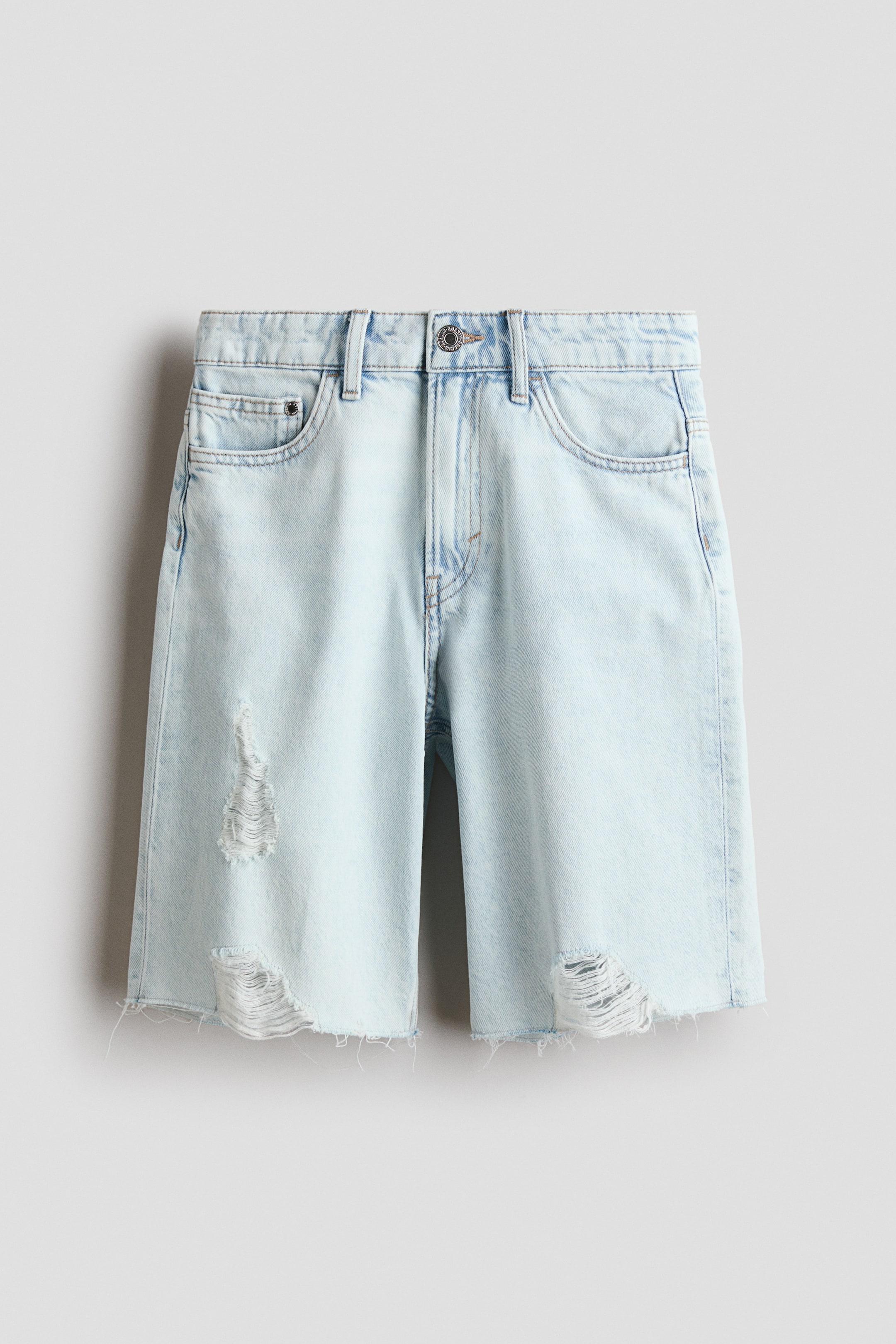 Agrandir l'image: Les shorts en denim bleu clair délavé présentent une coupe ample et une longueur au niveau des genoux à l'avant. Ils sont dotés d'une fermeture à bouton et zip, de passants pour ceinture, de deux poches avant, d'une poche à monnaie, ainsi que de détails usés sur les cuisses, avec des ourlets effilochés et bruts.