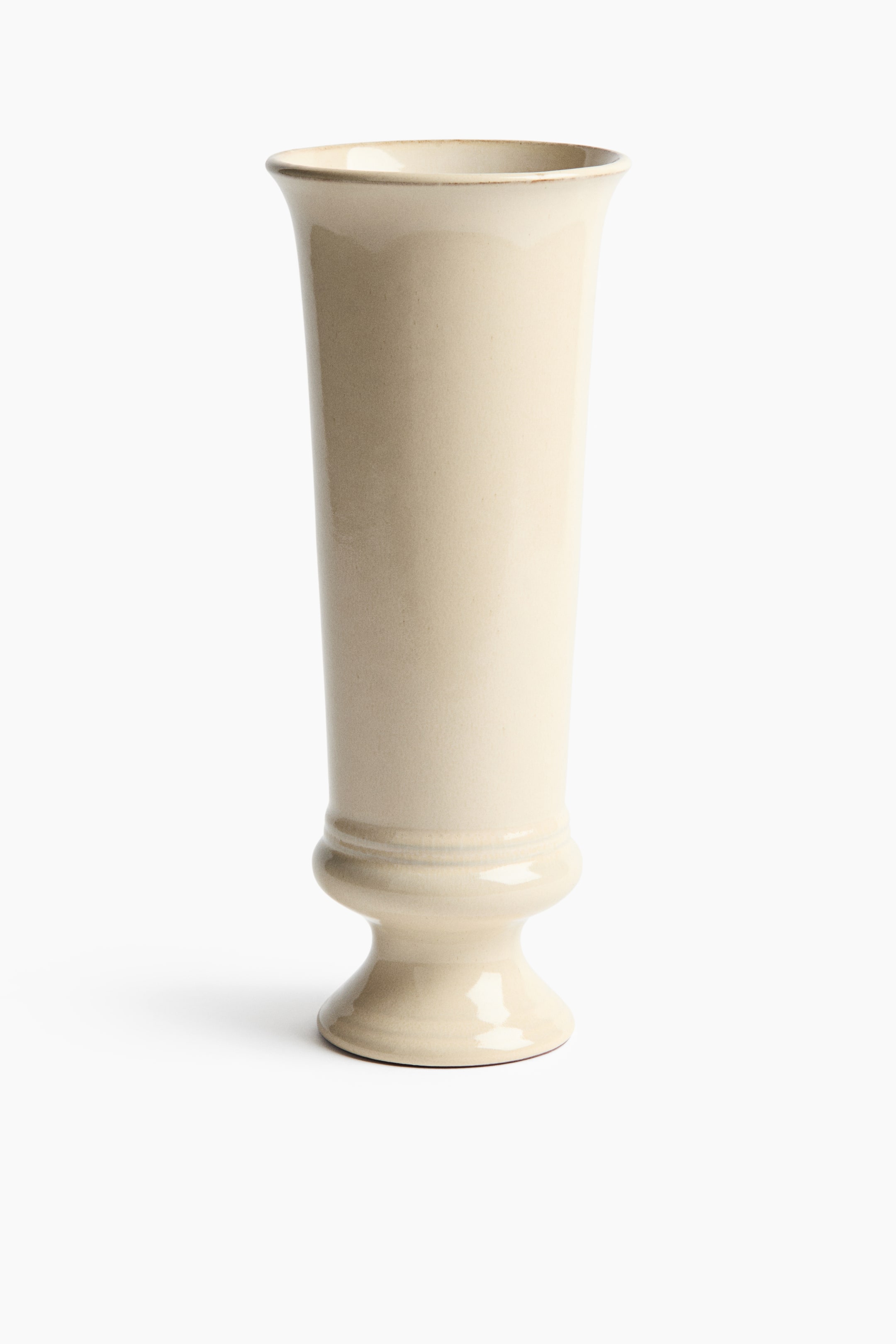 Grotere afbeelding bekijken: Een licht beige keramische vaas toont een lange, slanke vorm die zachtjes naar buiten uitwaaiert aan de bovenrand. De voetstukstijl basis heeft een afgerond, geribbeld gedeelte dat rust op een bredere, uitlopende voet.
