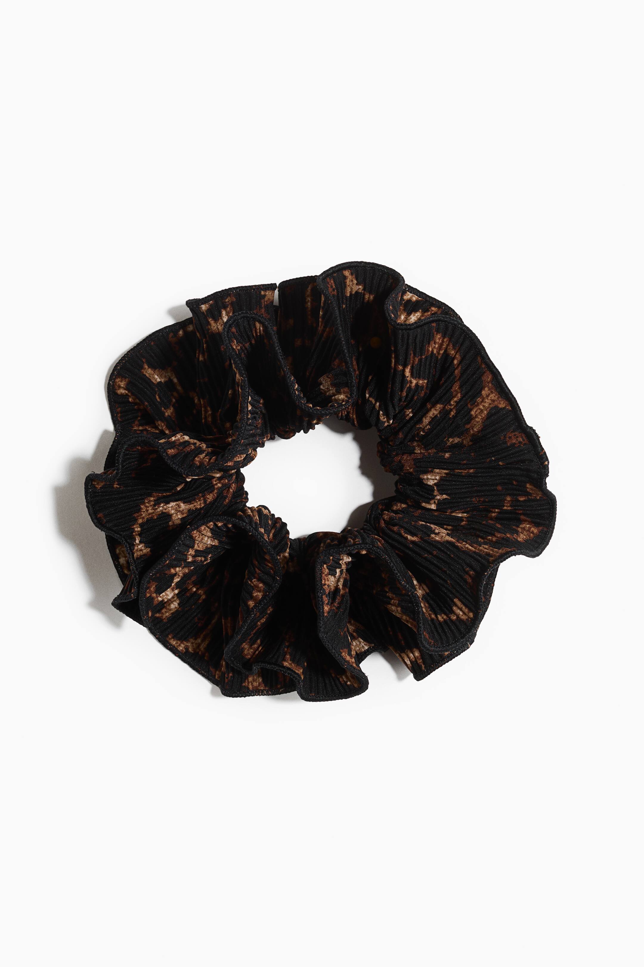 Zobrazit větší obrázek: Scrunchie má černo-hnědý zvířecí vzor. Nařasená látka vytváří objemný, volánový vzhled kolem jeho centrální elastické otvoru, když je prezentován naplocho.