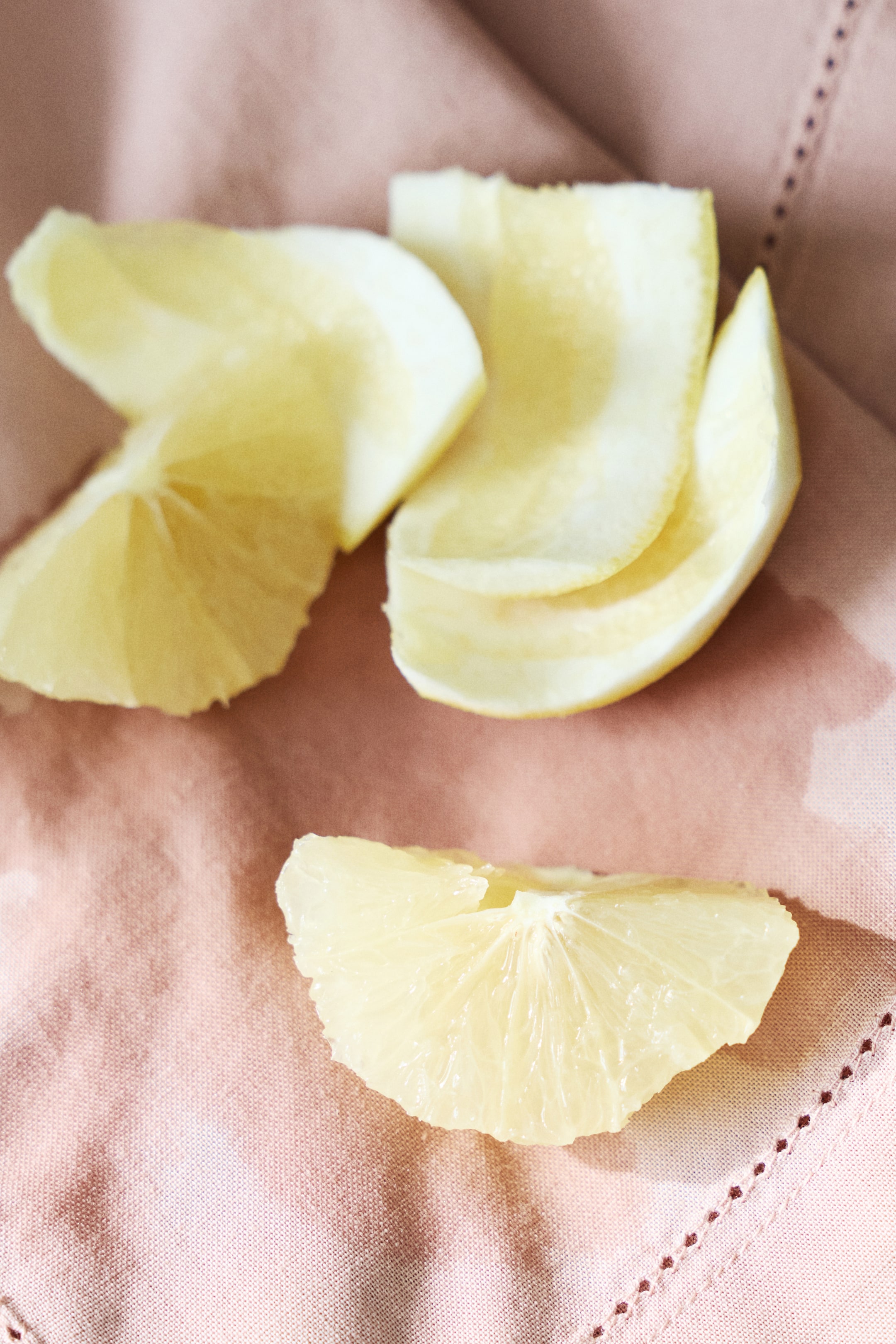 Zobacz większy obraz: Bladożółte plasterki cytryny ukazują swoją przezroczystą miąższ, wyraźne segmenty i cienką białą skórkę. Trzy klinowate plasterki leżą z przeciętymi powierzchniami skierowanymi ku górze.