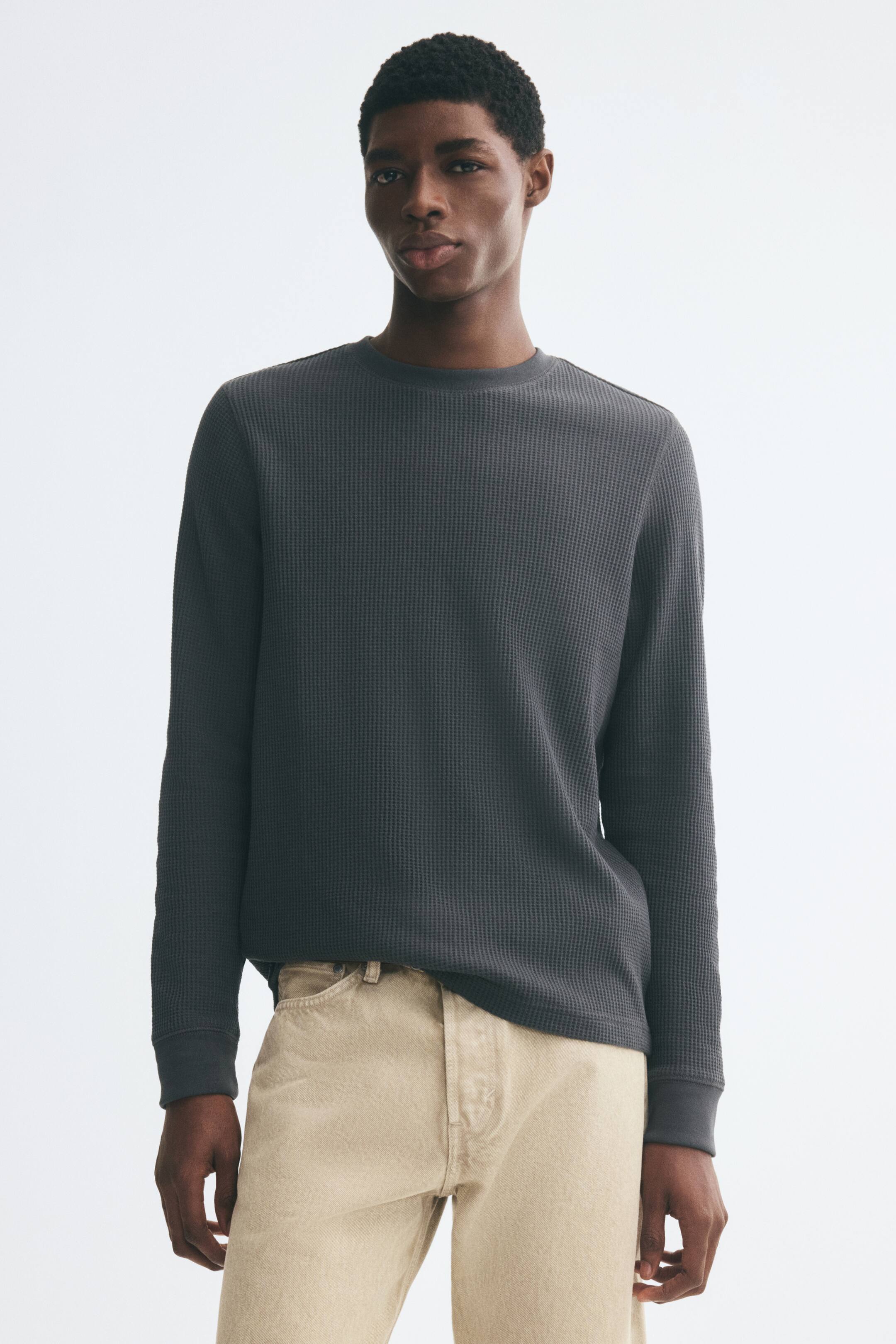 Voir une image plus grande: Un t-shirt à manches longues gris foncé en jersey de mélange coton gaufré est porté par le mannequin. Le haut présente un col rond côtelé et des poignets côtelés, et il est assorti à un jeans beige pâle.