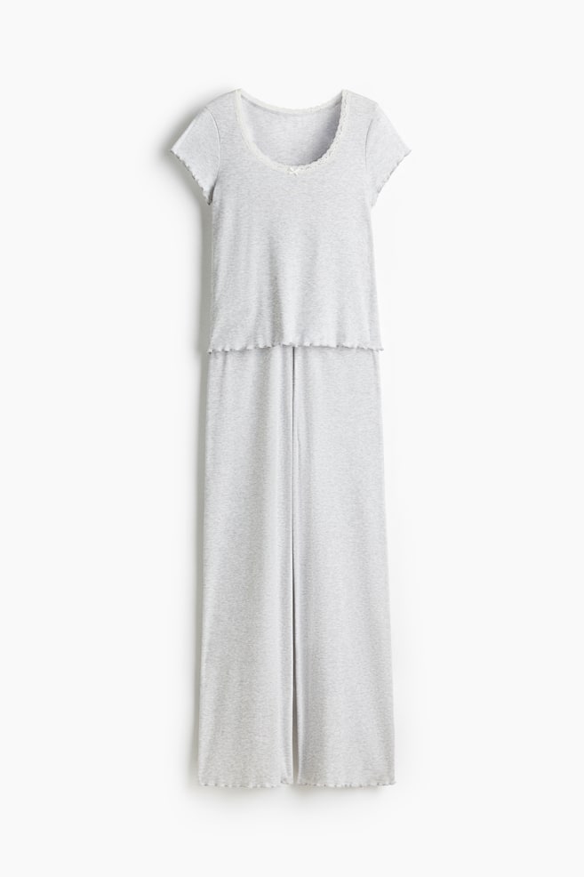 A FRONT view of a light grey, ribbed jersey pyjama set is displaying a short-sleeved top and long straight-leg bottoms. The top is featuring a deep, rounded neckline trimmed with white lace, and its short sleeves and hem are showing overlocked edges. The bottoms are displaying overlocked hems, with a small white decorative satin bow visible at the center front of the waistband. - 1
