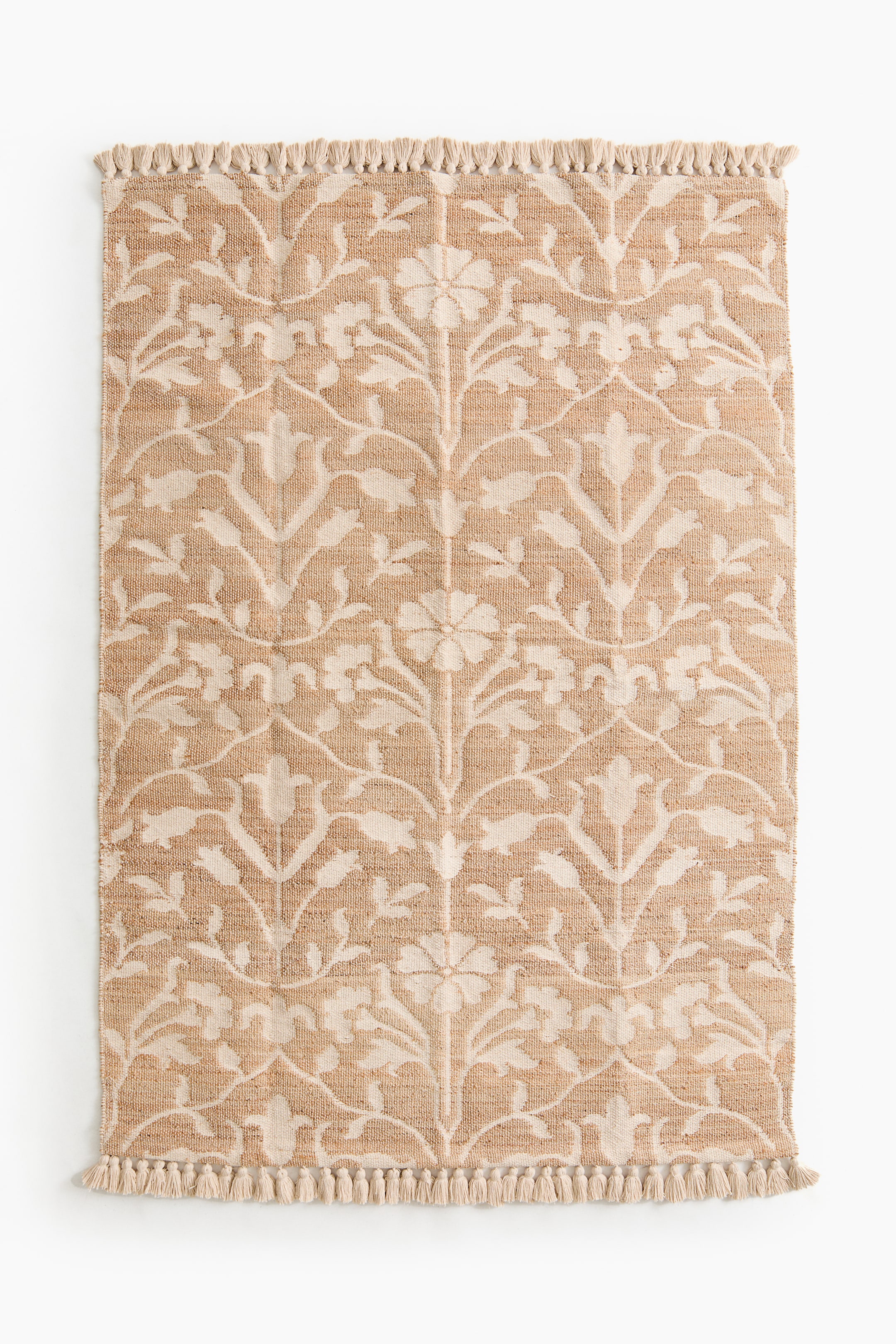 View larger image: The rug showcases a light-coloured floral pattern against a natural brown jute-and-cotton blend weave. It features fringes along its short ends.