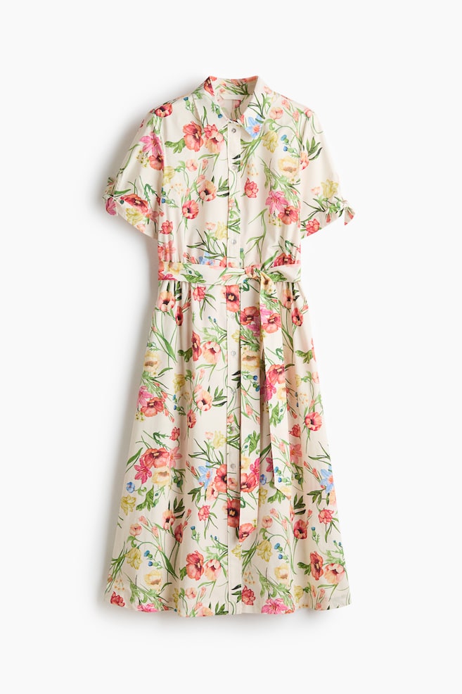 The calf-length dress is shown from the front, showcasing a colourful floral print on a light background, a collar, buttons down the front, short sleeves with ties at the cuffs, a gathered seam at the waist, a detachable tie belt, and a gently flared skirt. - 1