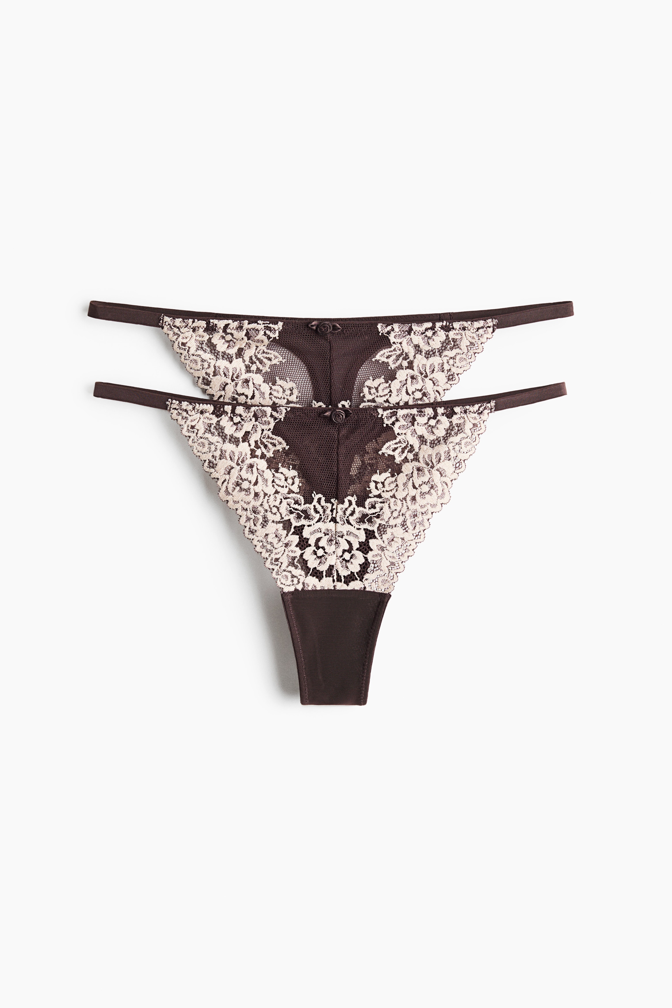 Ein G-String aus dunkelbraunem Mesh und weiÃer floraler Spitze wird aus der Vorderansicht getragen und zeigt seinen Low-Rise-Bund sowie die schmalen SeitenbÃ¤nder. Dazu wird ein passender BÃ¼gel-BH mit demselben dunkelbraunen Mesh und einer Ãberlage aus weiÃer Spitze kombiniert.