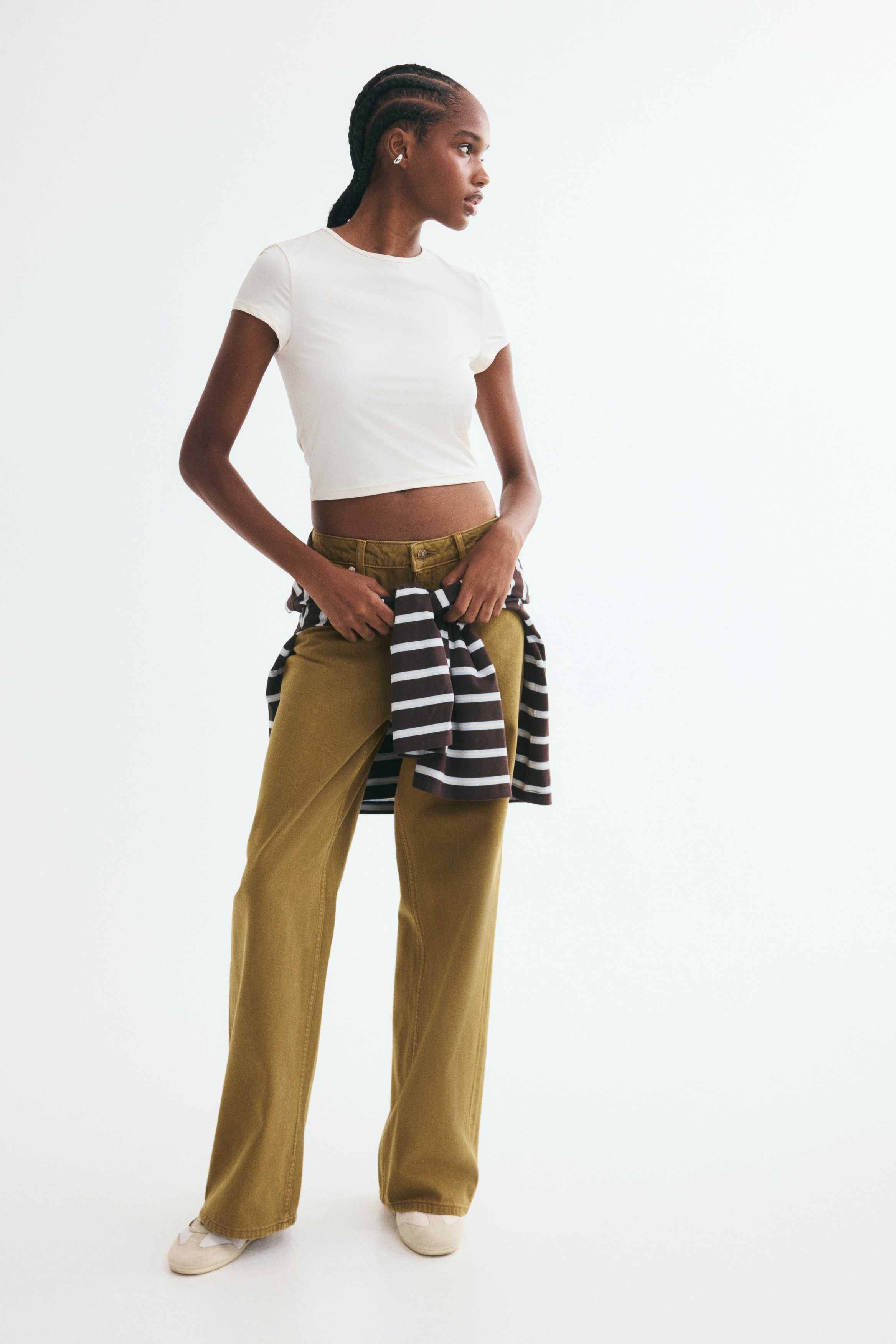 A pair of brown five-pocket jeans is shown from the front, featuring a regular waist with belt loops, a zip fly, and button fastening. The jeans have a loose, straight-leg silhouette with curved front pockets and metallic rivets.
