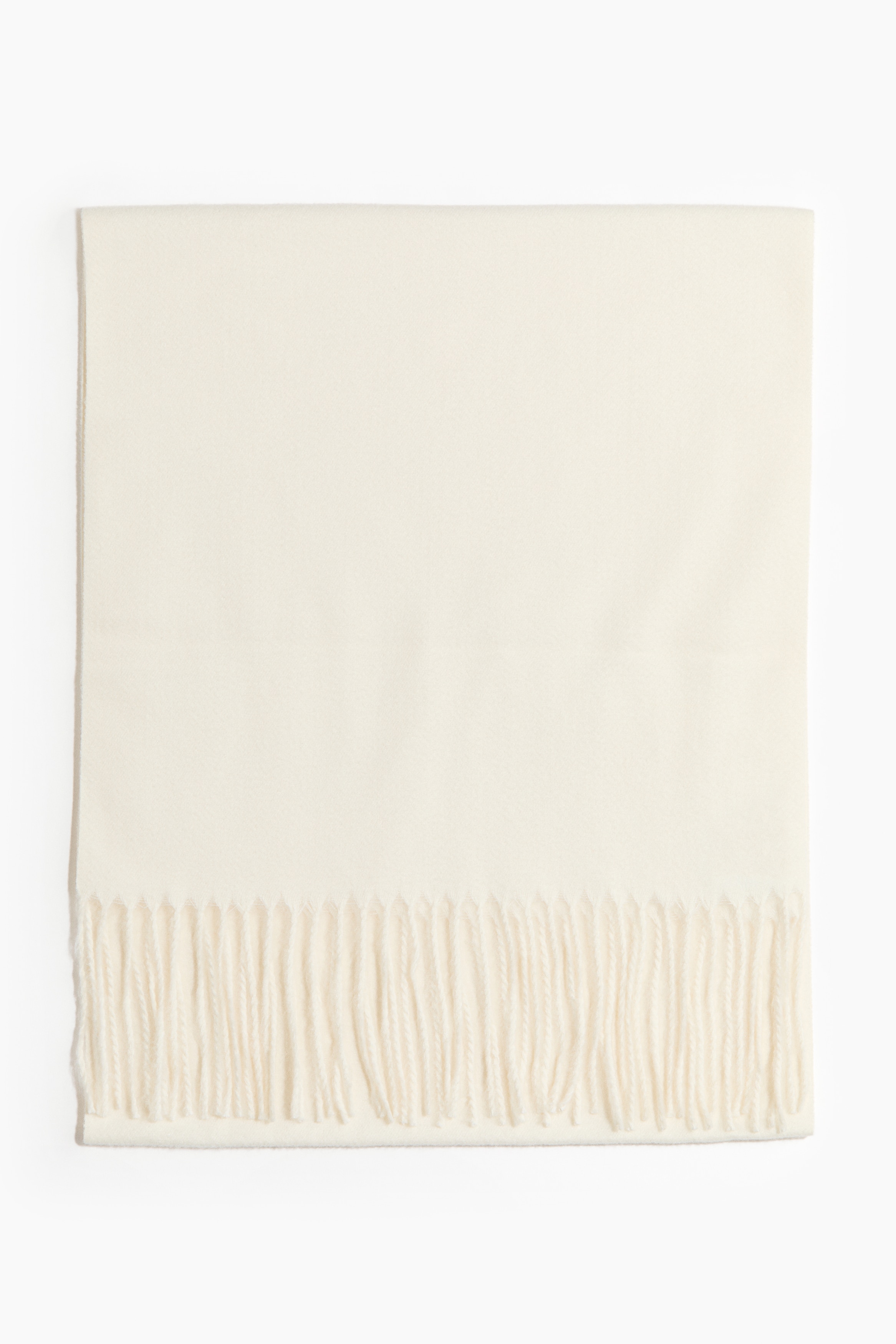 Ein cremefarbener Schal in weicher Webstruktur mit Fransen an den kurzen Seiten wird vom Model getragen, locker um den Hals gelegt und über einem passenden weichen Strickpullover geschichtet. Ein Ende des Schals ist um den Hals gewickelt, während die andere Seite vorne herabhängt und so die Fransenkante betont.