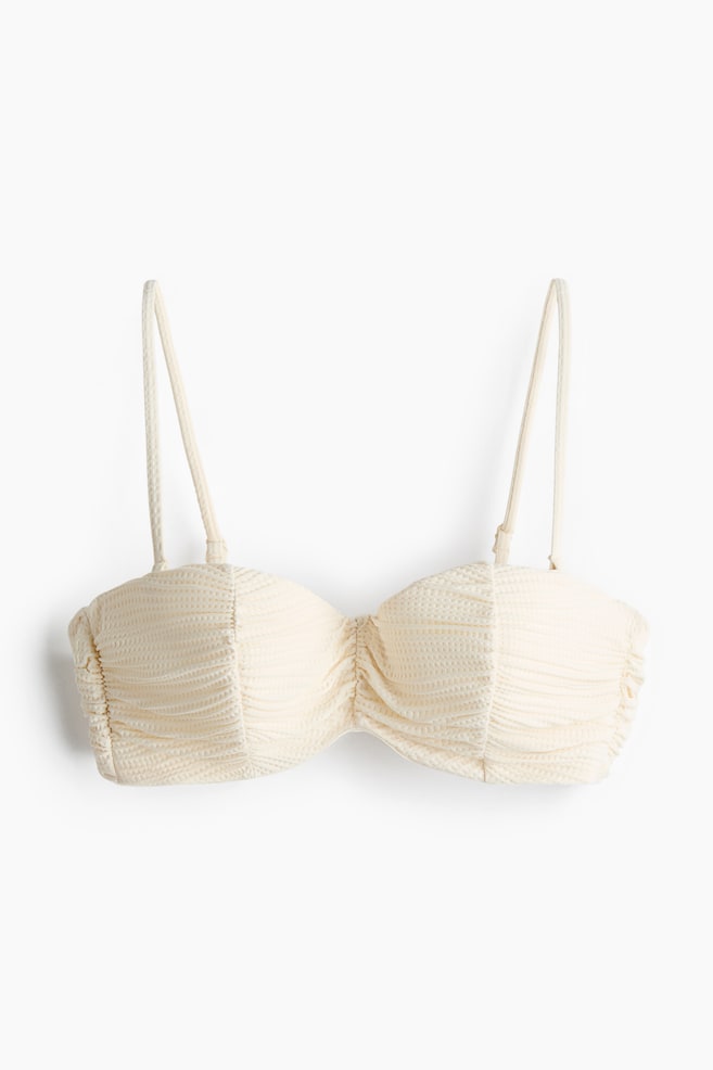 A cream-coloured bandeau bikini top features a textured waffle-knit fabric. Shirring is visible at the centre and sides of the cups, with thin adjustable spaghetti straps. - 1