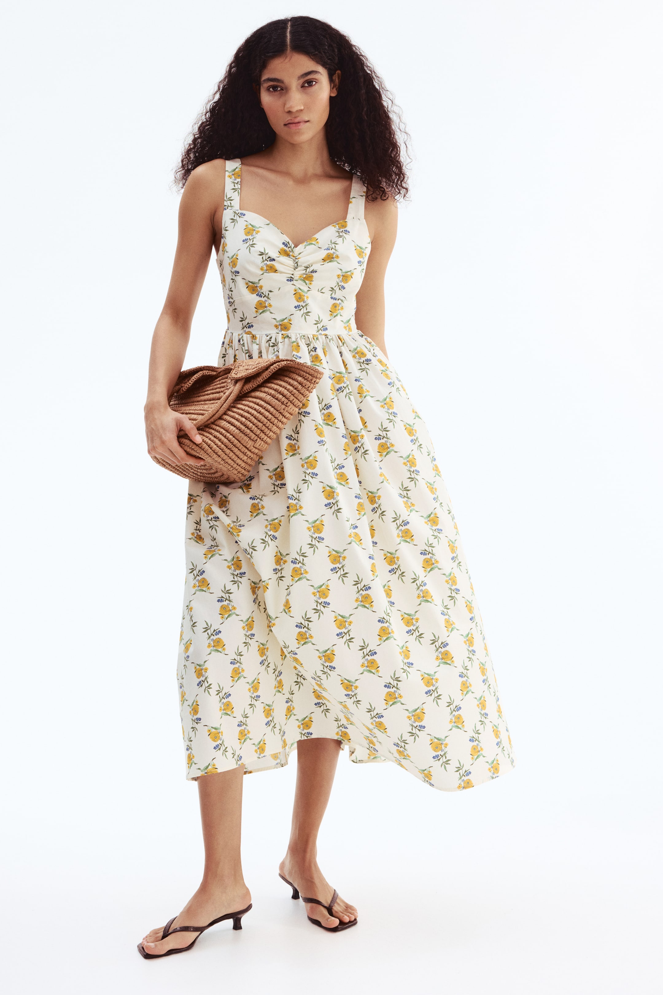 View larger image: A white midi dress featuring a repeating pattern of yellow roses and blue leaf sprigs, wide shoulder straps, a sweetheart neckline with central ruching, and a gathered A-line skirt.