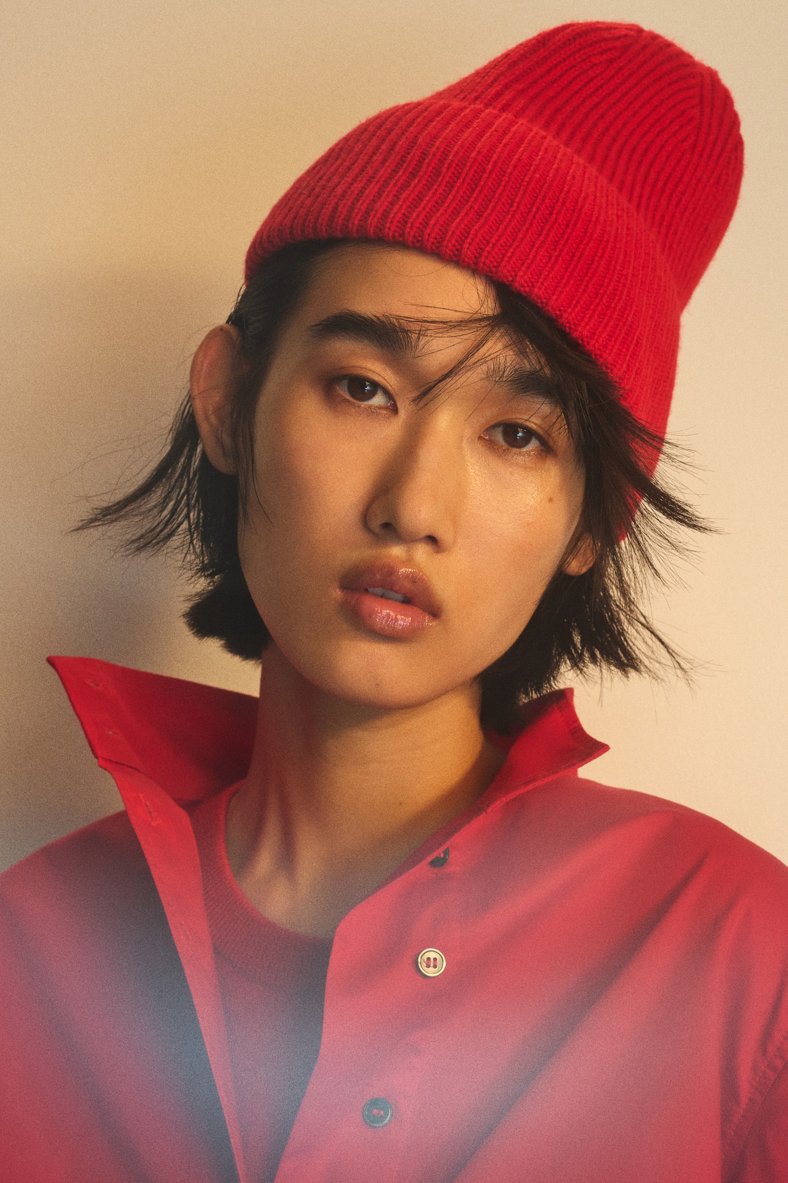 Eine leuchtend rote Beanie aus weichem Rippstrick mit umgeschlagenem Saum wird vom Model getragen. Die Beanie sitzt hoch auf dem Kopf und ist auf das rote Hemd mit Kragen abgestimmt. - 1
