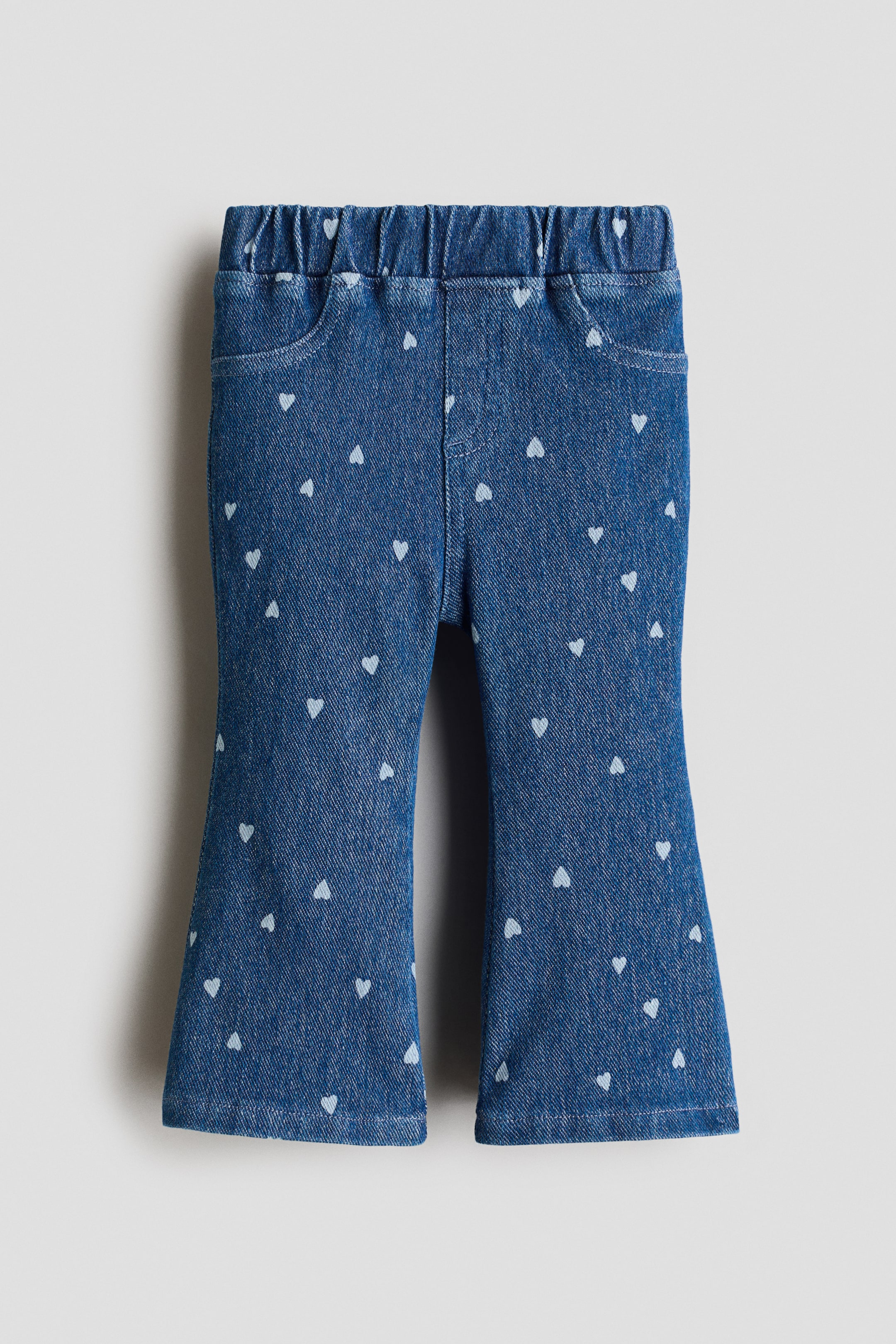 View larger image: Front-facing flared leggings in blue denim-look jersey featuring an elasticated waist, decorative front pockets, and an all-over pattern of small white hearts.