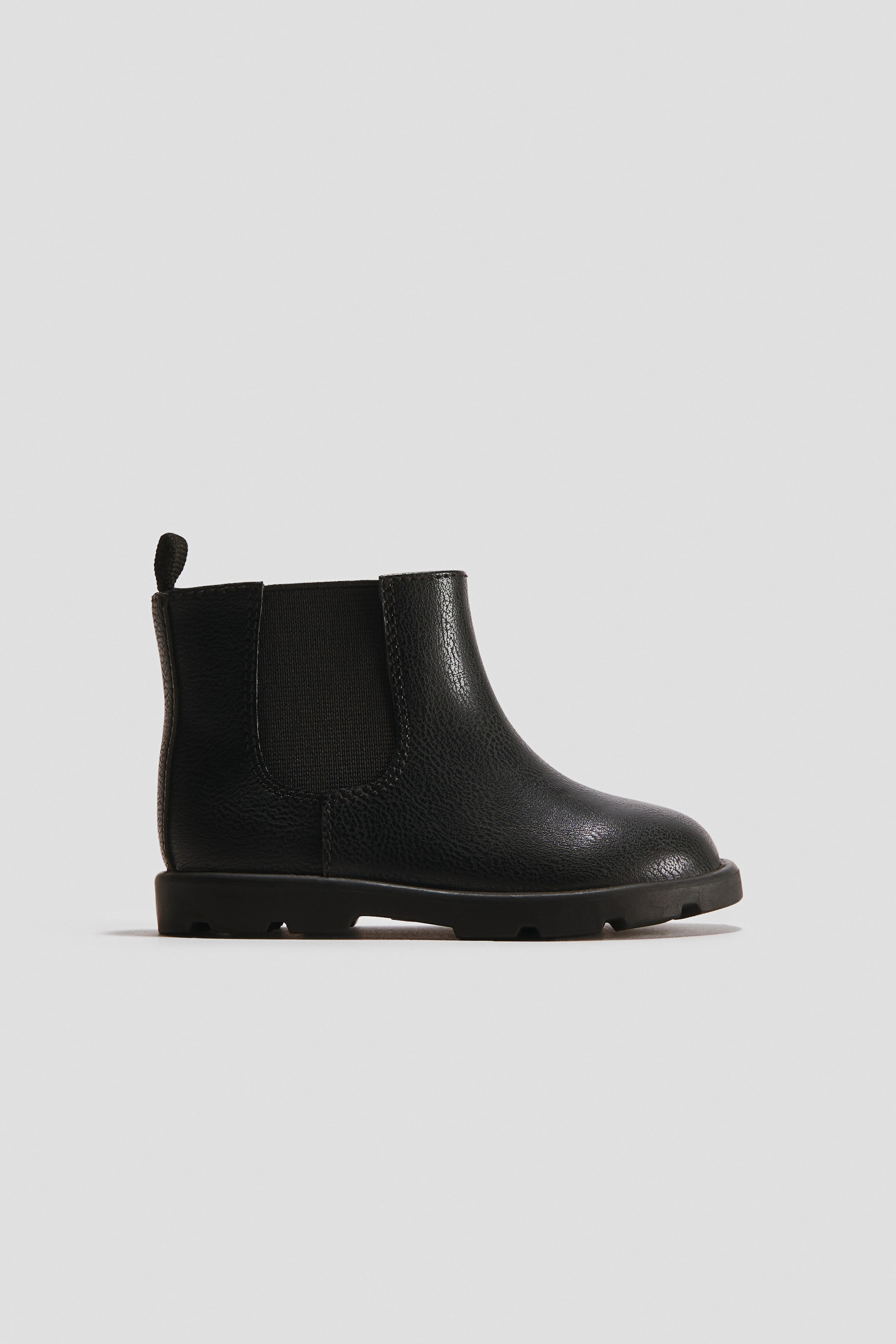 Grotere afbeelding bekijken: Een zwarte Chelsea-boot toont zijn zijprofiel, met een gestructureerd bovenwerk, een elastisch zijpaneel, een treklus aan de achterkant en een robuuste zool.