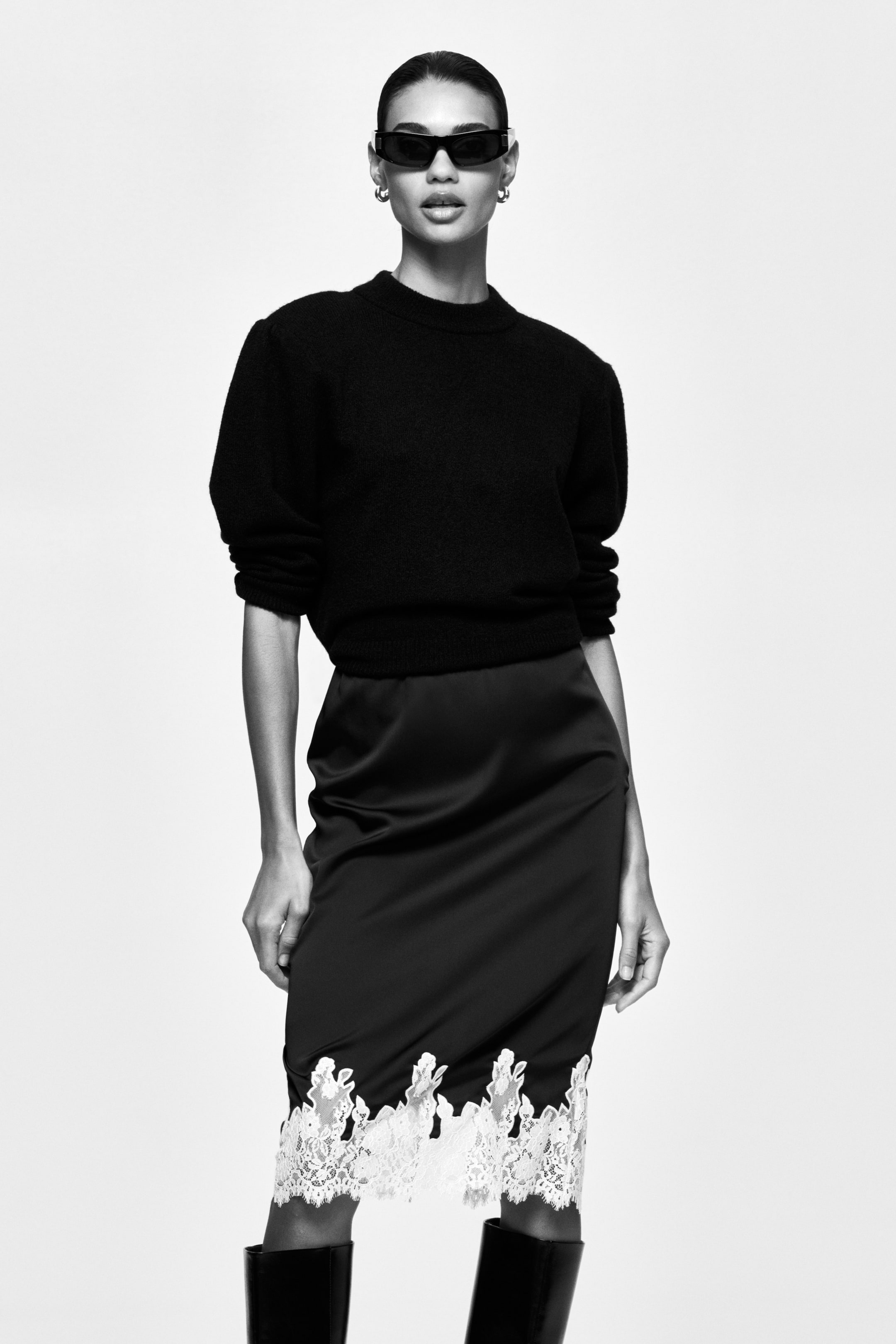 View larger image: The model is showcasing a black knit jumper, characterised by a high, round neckline and structured shoulders. It features 3/4-length sleeves with volume at the top, complemented by rib-knit trim at the neckline, cuffs, and hem, styled over a dark skirt.