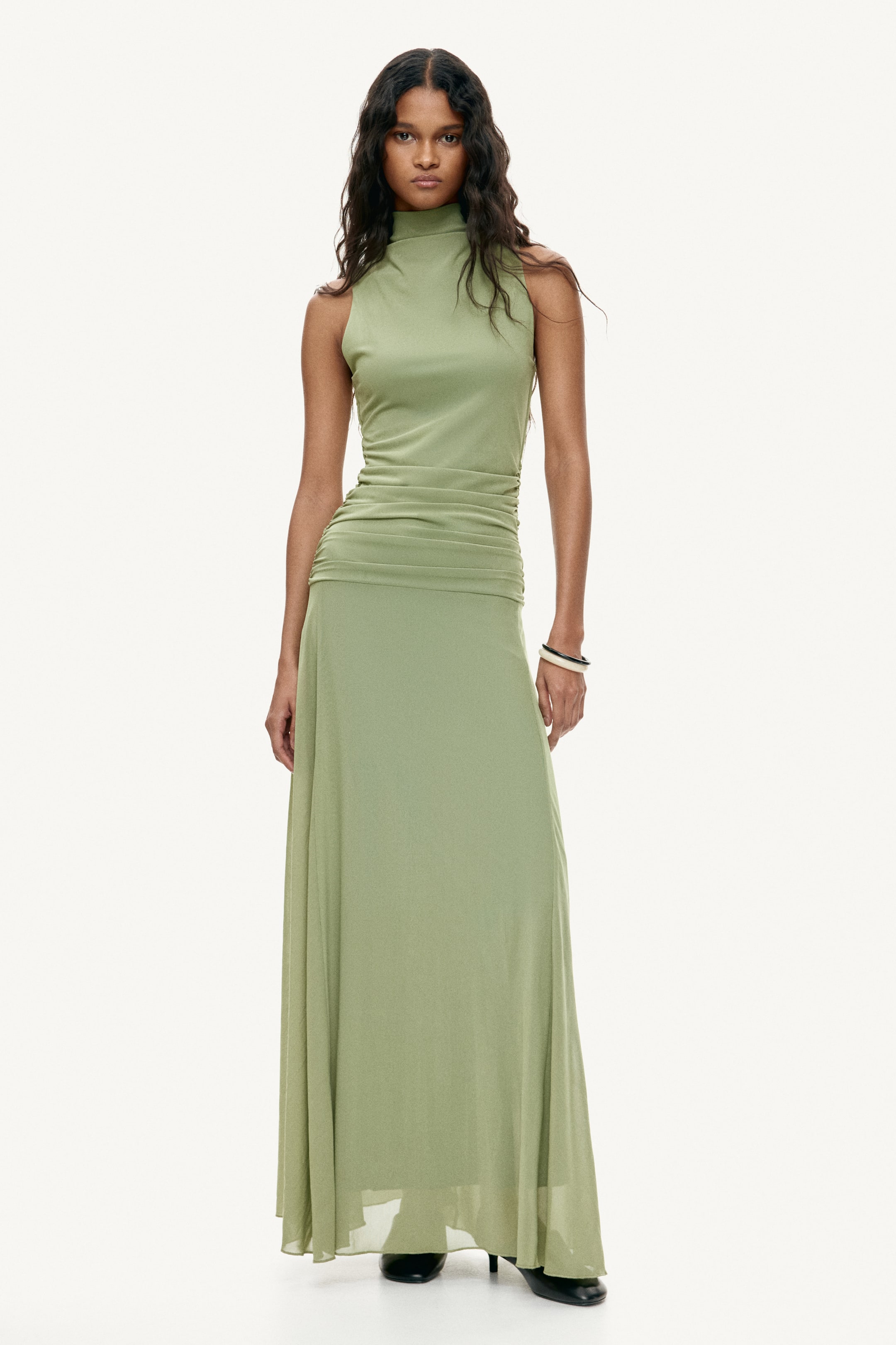 Grotere afbeelding bekijken: De lichtgroene mouwloze jurk, van voren gezien, heeft een opstaande kraag en een aansluitend lijfje met geplooide details in het midden. De maxi-rok valt soepel.