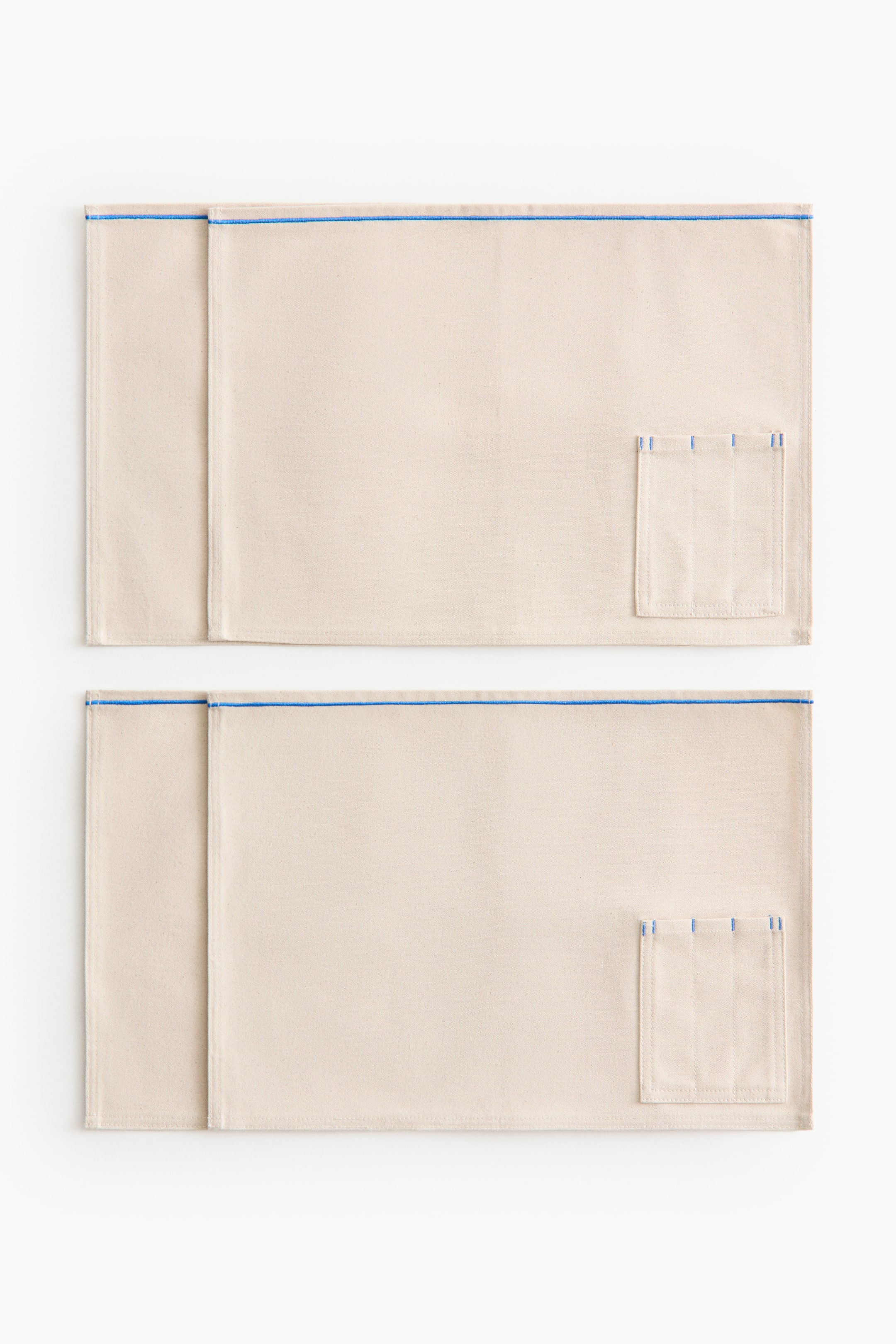 View larger image: Two light beige rectangular fabric mats are displayed facing forward. Each mat features a blue horizontal stitch line near the top edge and a small patch pocket on the right side, detailed with several vertical blue stitch lines along the top.