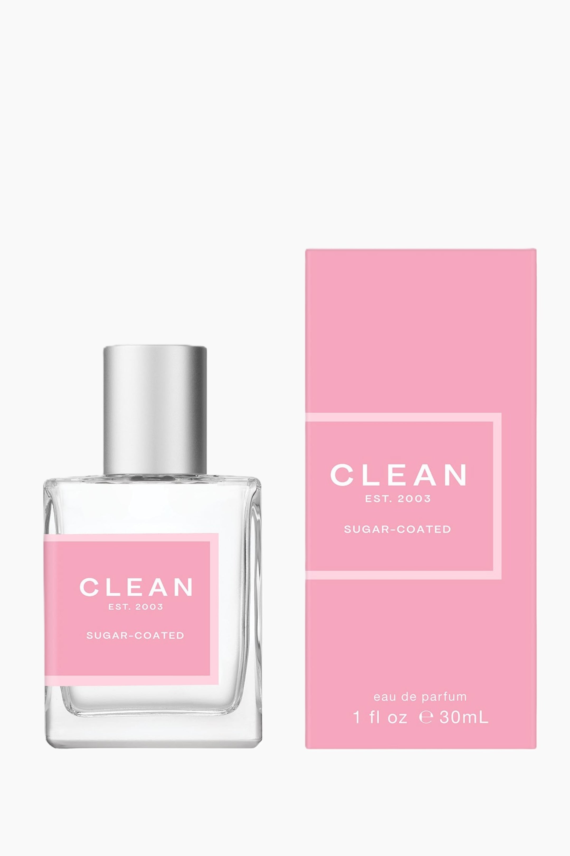 Se større billede: En klar glasparfumeflaske med en sølvtonet hætte står ved siden af en matchende lyserød rektangulær æske. Flasken har en lyserød etiket med teksten 'CLEAN EST. 2003 SUGAR-COATED,' mens æsken viser samme tekst sammen med 'eau de parfum 1 fl oz e 30mL.'