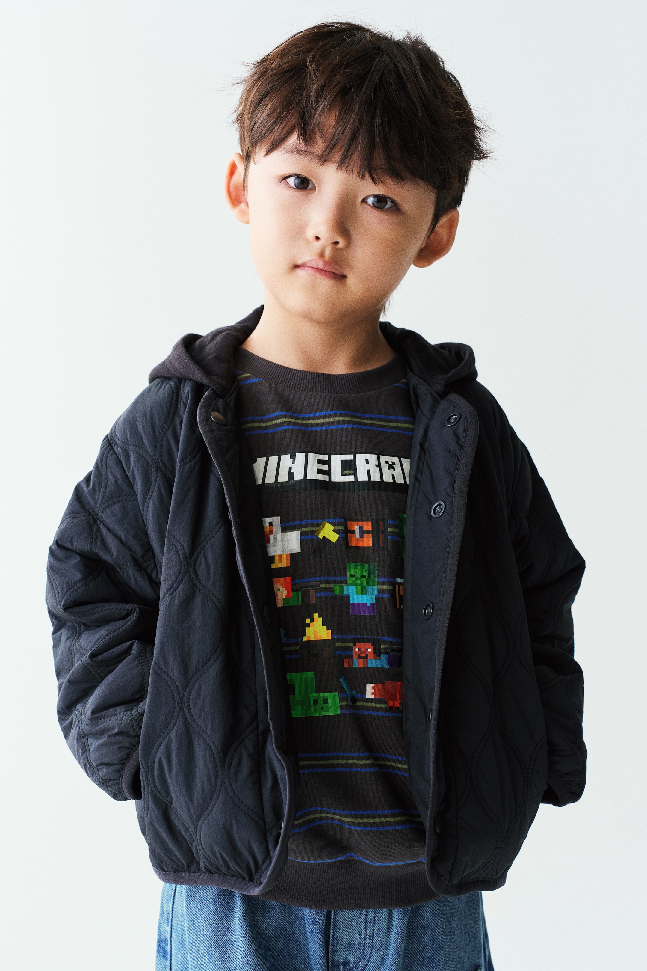 이미지 확대 보기: 모델이 검정색 퀼팅 재킷을 오픈한 상태로 착용하고 있으며, 안에는 짙은 회색 그래픽 스웨트셔츠와 청바지를 레이어드했습니다. 재킷은 양파 퀼팅 패턴, 버튼 여밈, 여유로운 핏이 특징입니다.