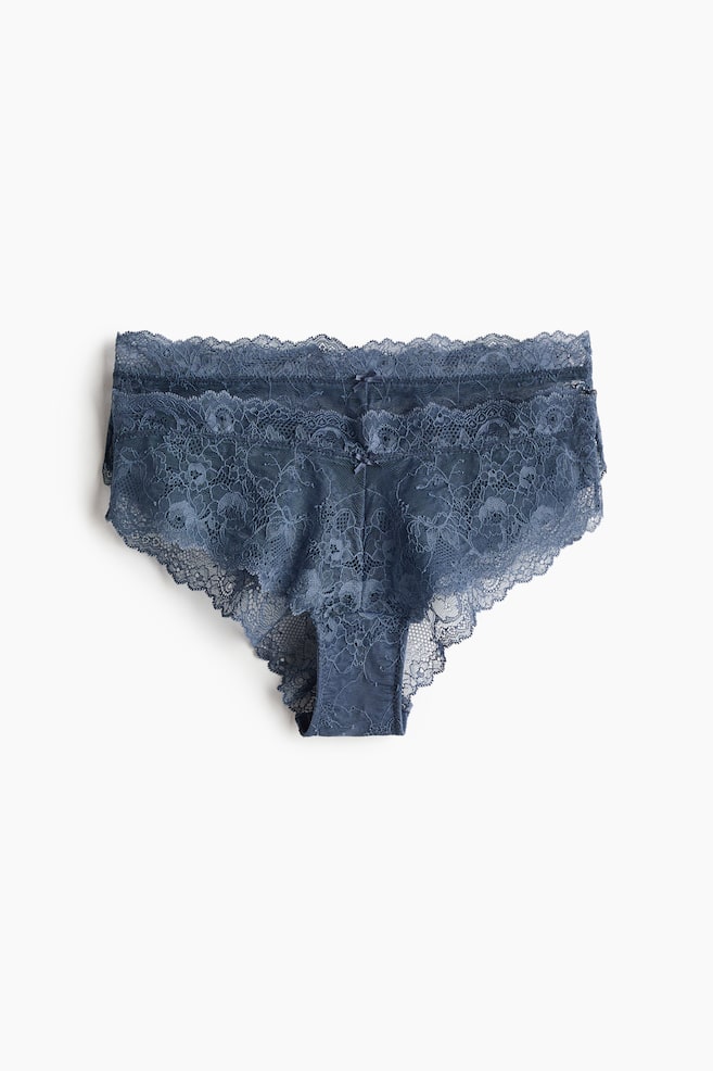 Ein Paar dunkelblaue Spitzen-Slips liegt flach und ist von vorne zu sehen. Es zeigt ein florales Spitzenmuster mit gewellten Kanten entlang der Taille und Beinöffnungen. Kleine Schleifendetails zieren den vorderen Bund. - 1