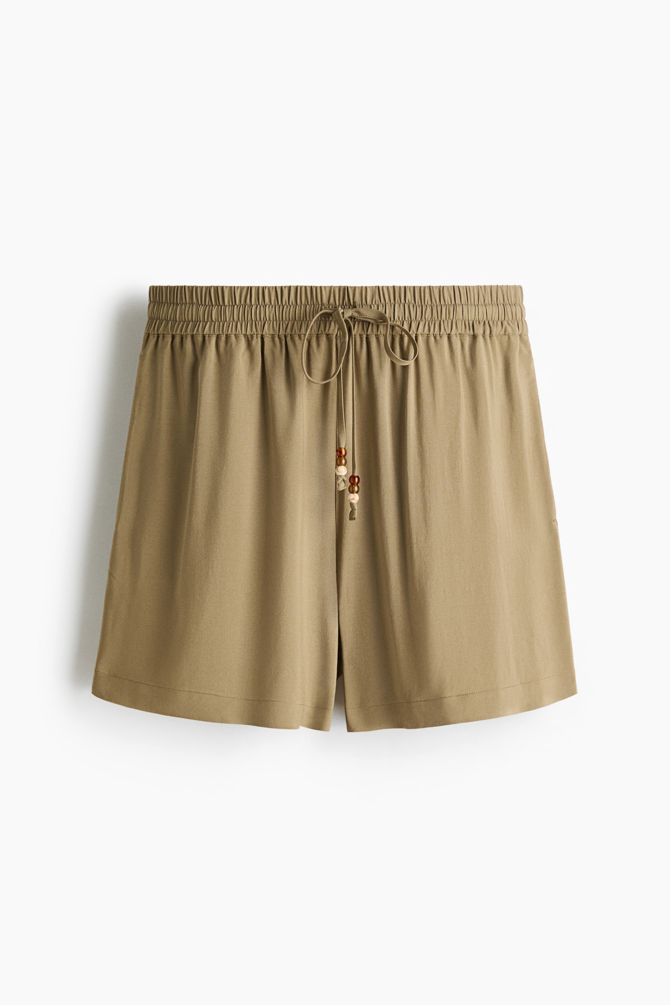 View larger image: Khaki shorts feature an elasticated, gathered front waistband. A drawstring, tied in a bow and adorned with decorative beads, extends from the centre of the waistband.