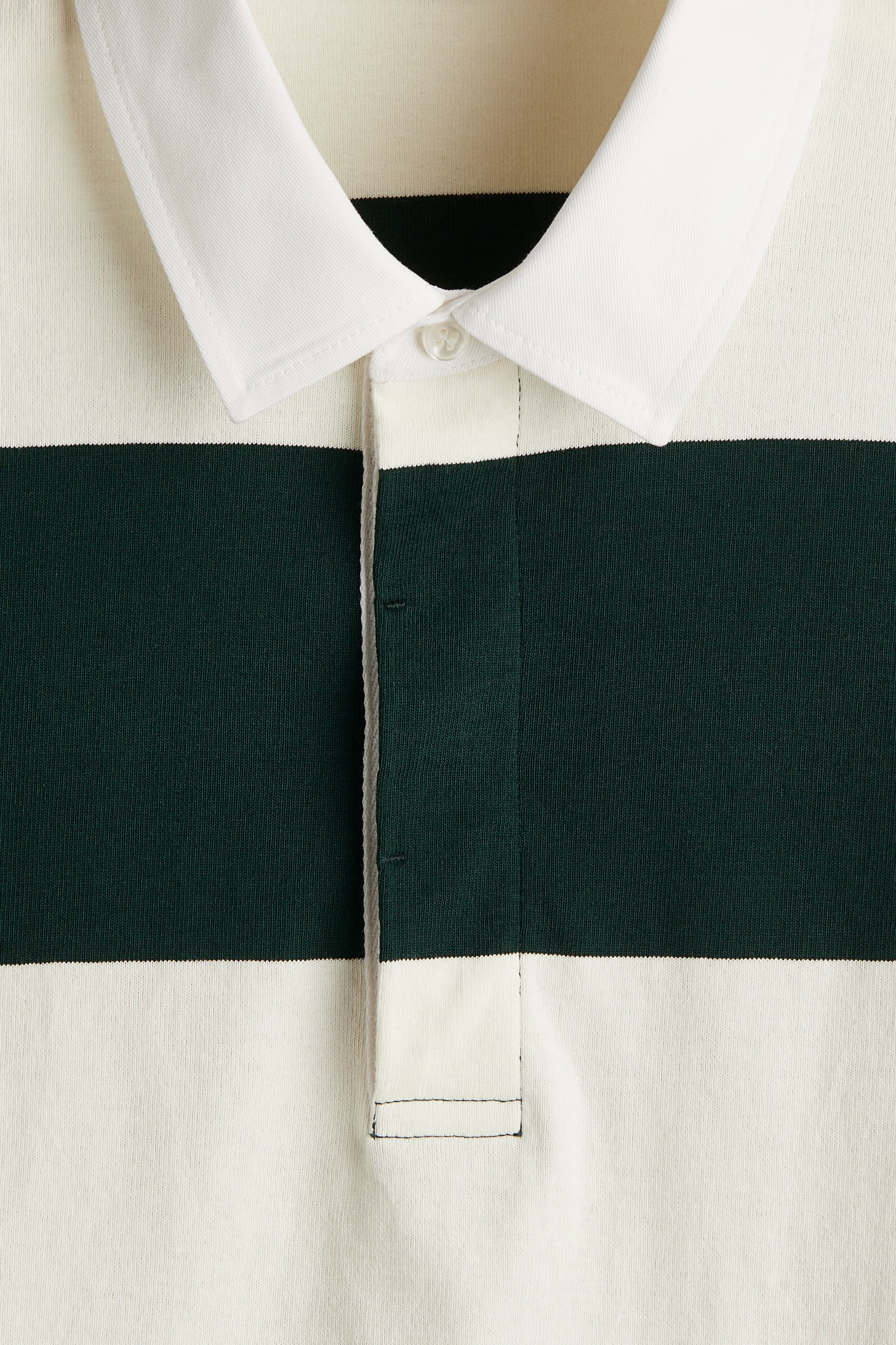 View larger image: A polo shirt is being presented from the front, featuring wide horizontal stripes in off-white and dark green, a white collar, and a two-button placket with one white button currently fastened.