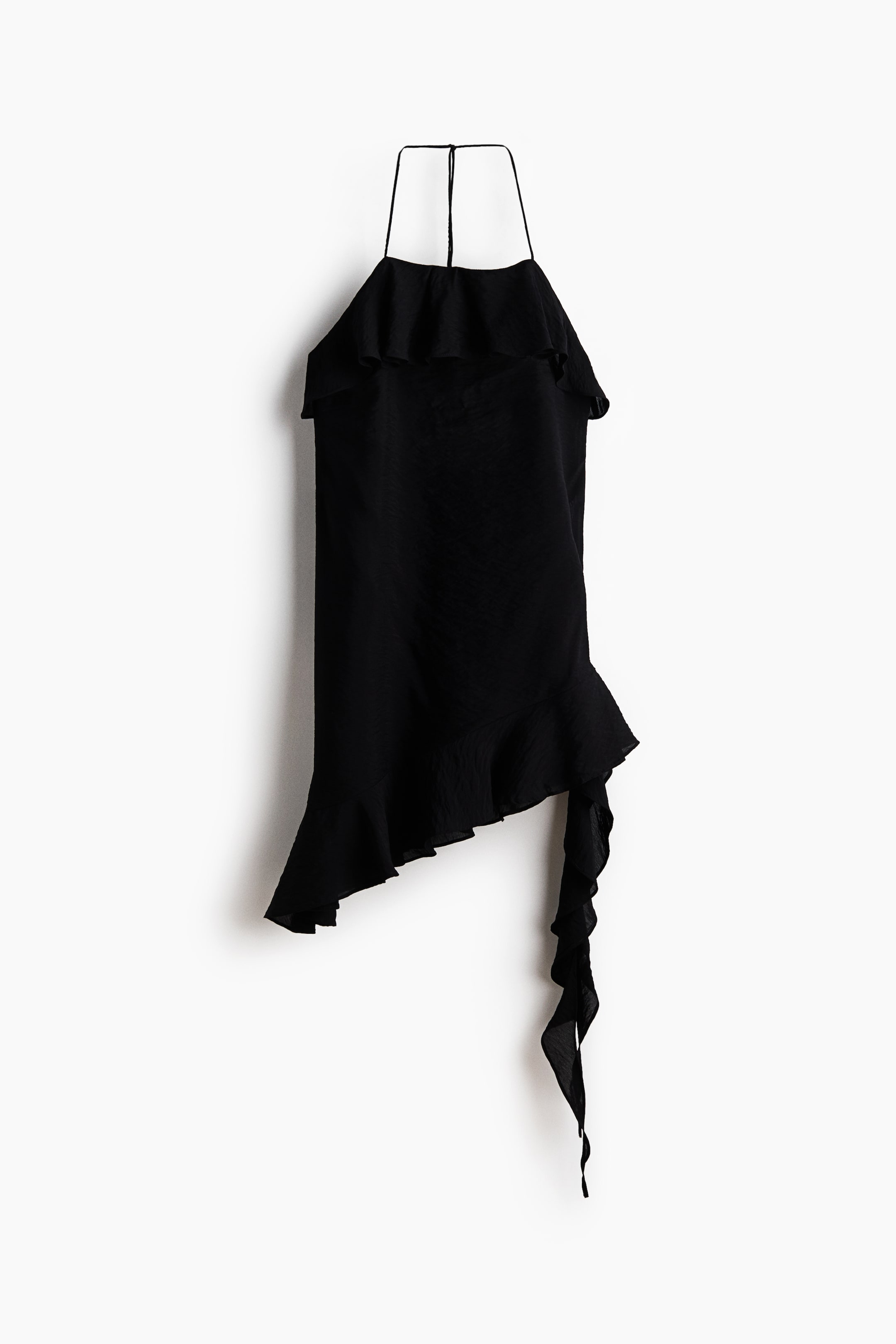 Ampliar la imagen: Un top negro de cuello halter se muestra en vista frontal, con tirantes delgados y un amplio volante en el busto que se extiende sobre los hombros. Su cuerpo suelto termina en un dobladillo asimétrico, adornado con un volante que continúa en una tira de tela larga y rizada en el lado derecho.