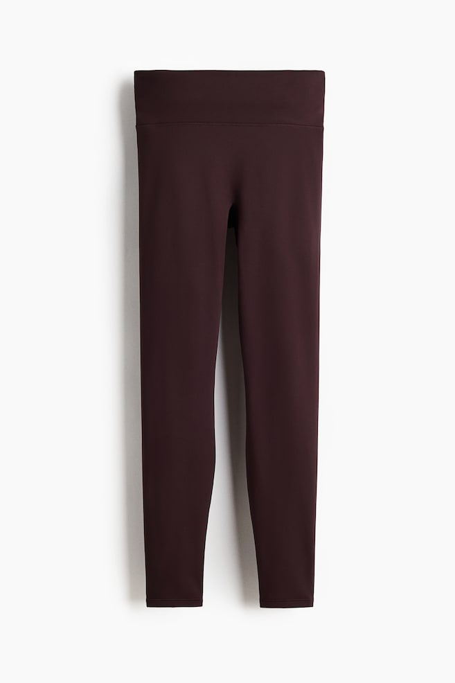 A pair of dark burgundy leggings is hanging, showcasing its front. It features a wide, high-rise waistband and smooth, full-length legs. - 1