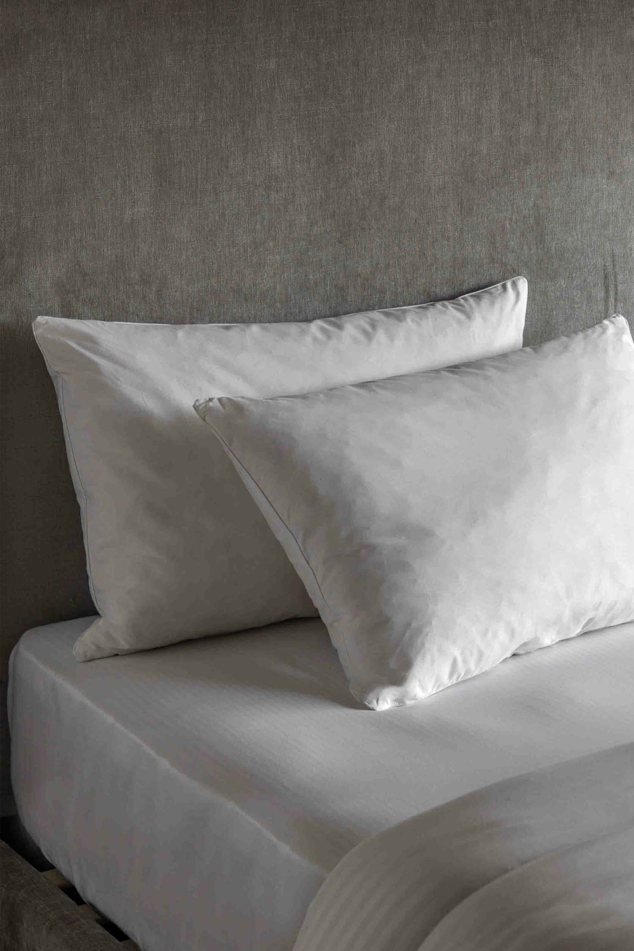 View larger image: Two white pillows are resting upright on a white fitted sheet, with one pillow positioned slightly in front of the other and angled forward. Both pillows are covered in smooth, white pillowcases, and the fitted sheet is displaying subtle vertical stripes.