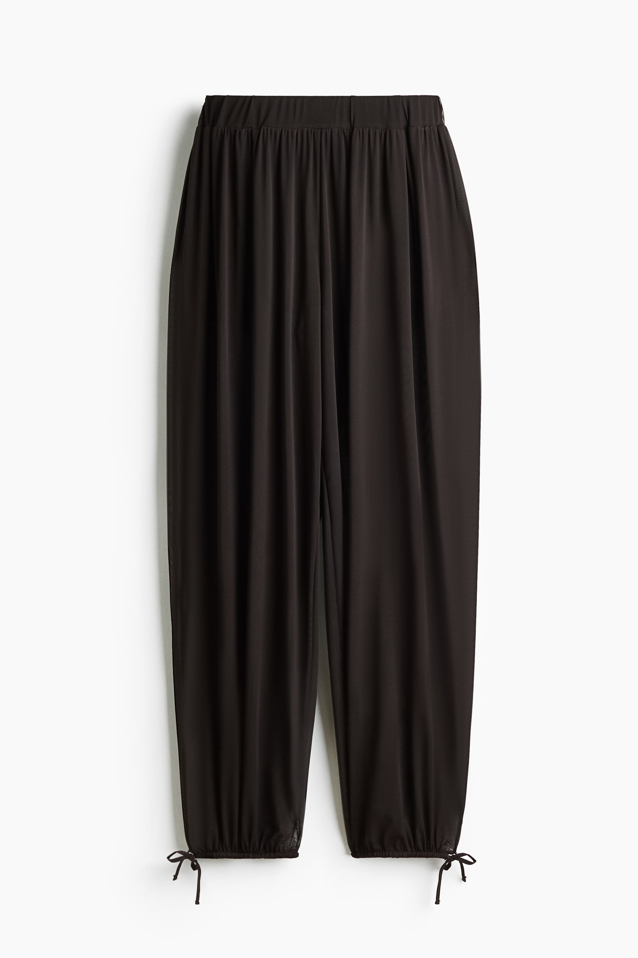 Ver imagen más grande: Los pantalones negros presentan una cintura elástica fruncida y piernas sueltas de largo completo. Las aberturas de las piernas se recogen en los tobillos con cordones atados en pequeños lazos, y un sutil detalle de malla es visible en el dobladillo inferior.