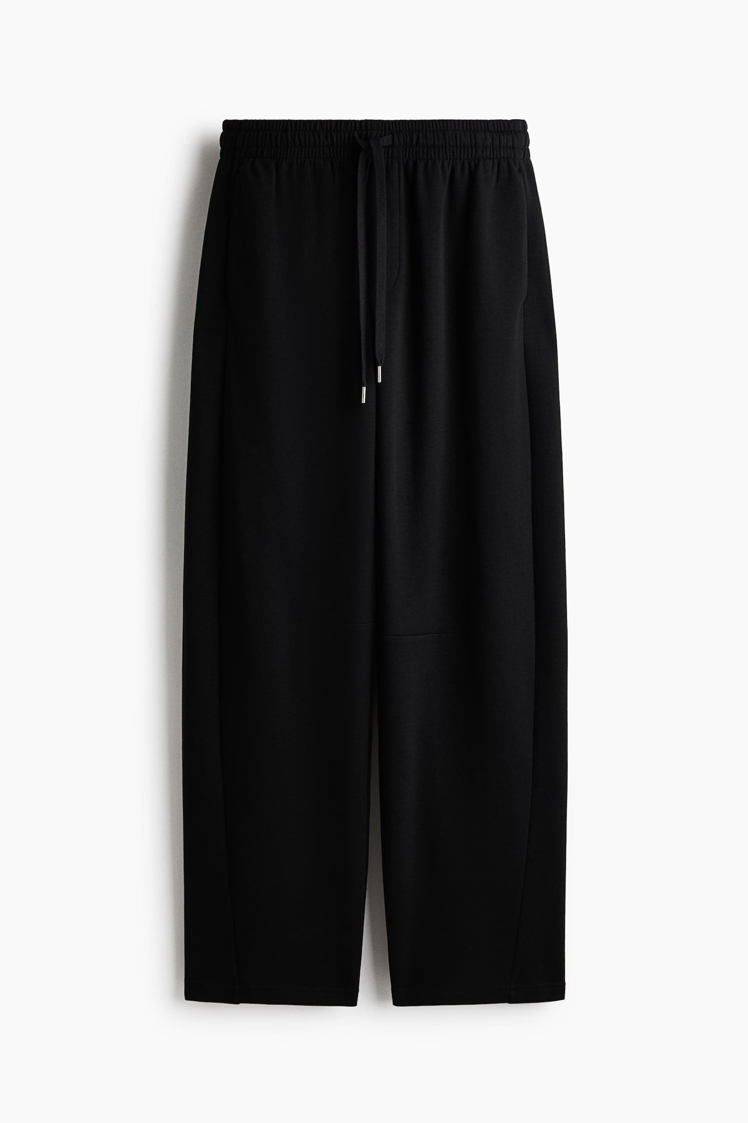 Schwarze Jogger mit lockerem Schnitt hÃ¤ngen frontal und verfÃ¼gen Ã¼ber einen hohen, elastischen Bund mit Kordelzug und Metallenden. Die Jogger zeigen eine lÃ¤ssige Barrel-Leg-Silhouette mit Fake-Fly-Detail und dezenten Seitentaschen.
