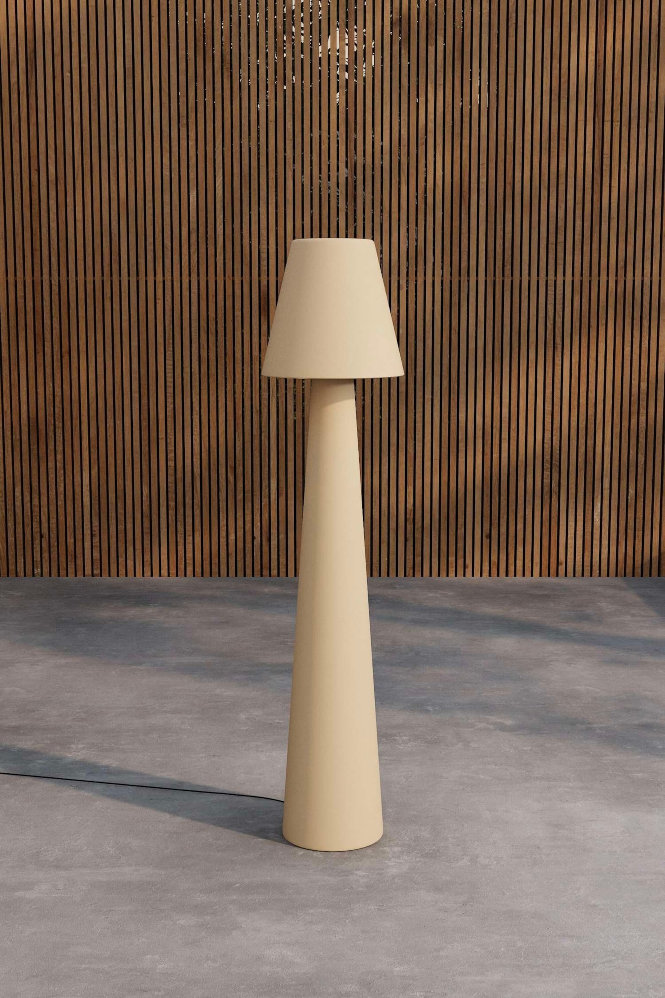 Agrandir l'image: Une lampe sur pied de couleur crème se tient droite, avec un corps unique formant une large base conique qui se rétrécit en une tige cylindrique plus étroite. Un abat-jour assorti et effilé repose sur le sommet de la tige, et un cordon d'alimentation noir s'étend depuis la base de la lampe.