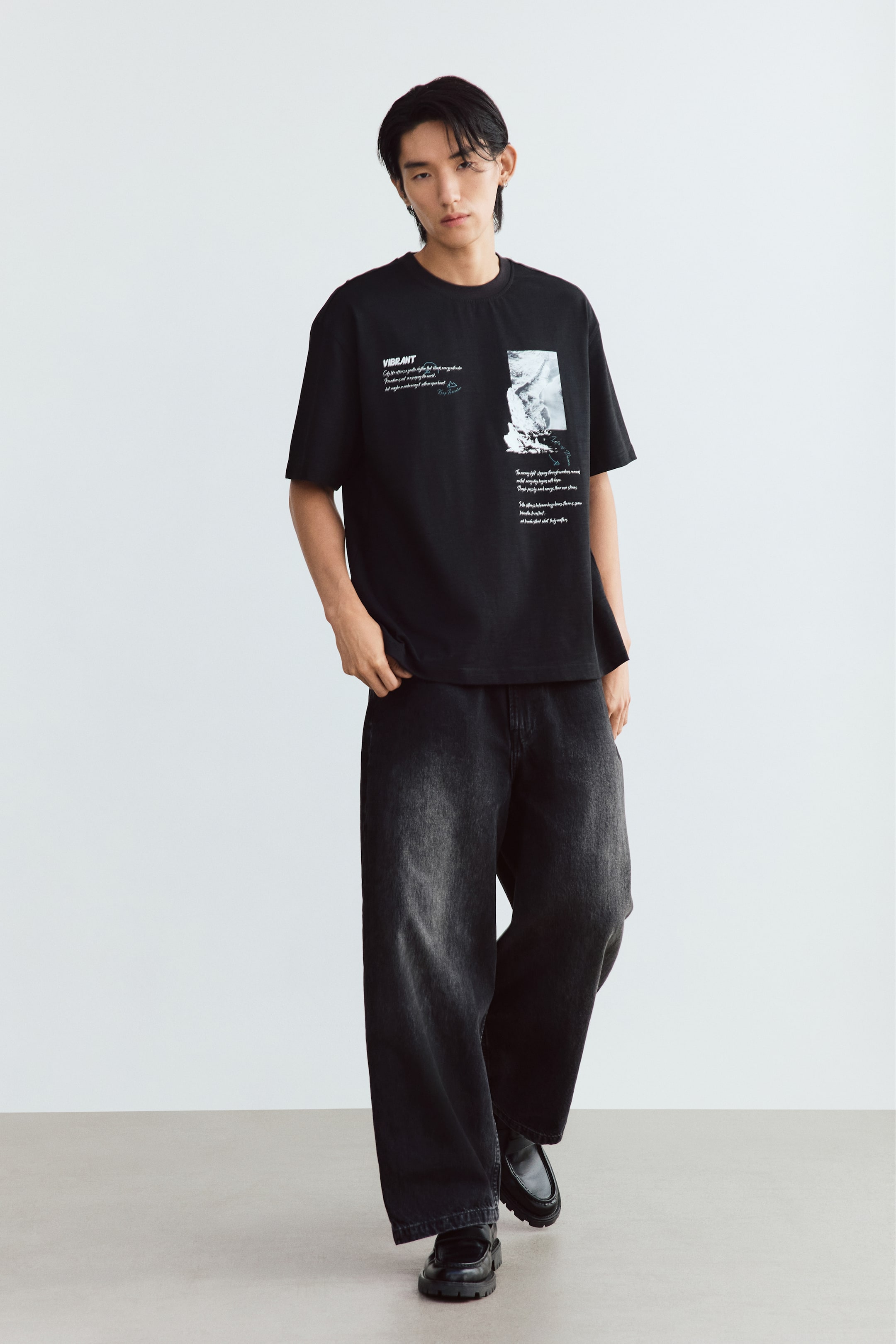 查看大圖: 模特兒正穿著一件黑色棉質 jersey T 恤，正面印有白色圖案及文字。這件寬鬆剪裁上衣採用下墜肩設計、圓領羅紋領口及直腳下擺，並配搭寬褲腳深色水洗牛仔褲。