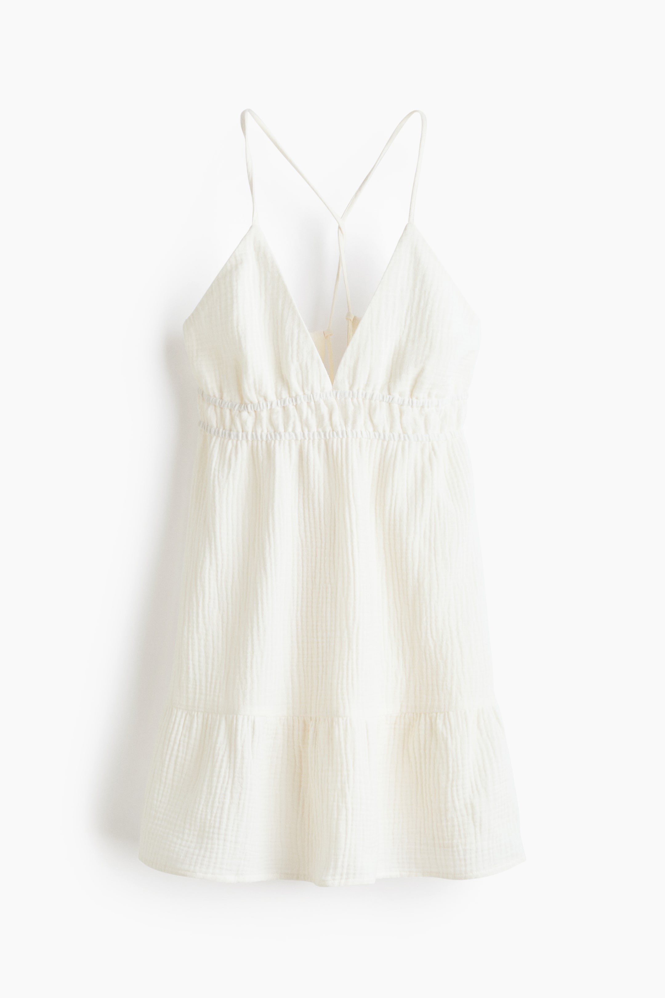 Ver imagen más grande: Un vestido mini de gasa arrugada en color blanco roto es visible desde el frente, con un escote en V, finos tirantes espagueti cruzados en la espalda, cintura elástica fruncida y un volante escalonado sobre el dobladillo.