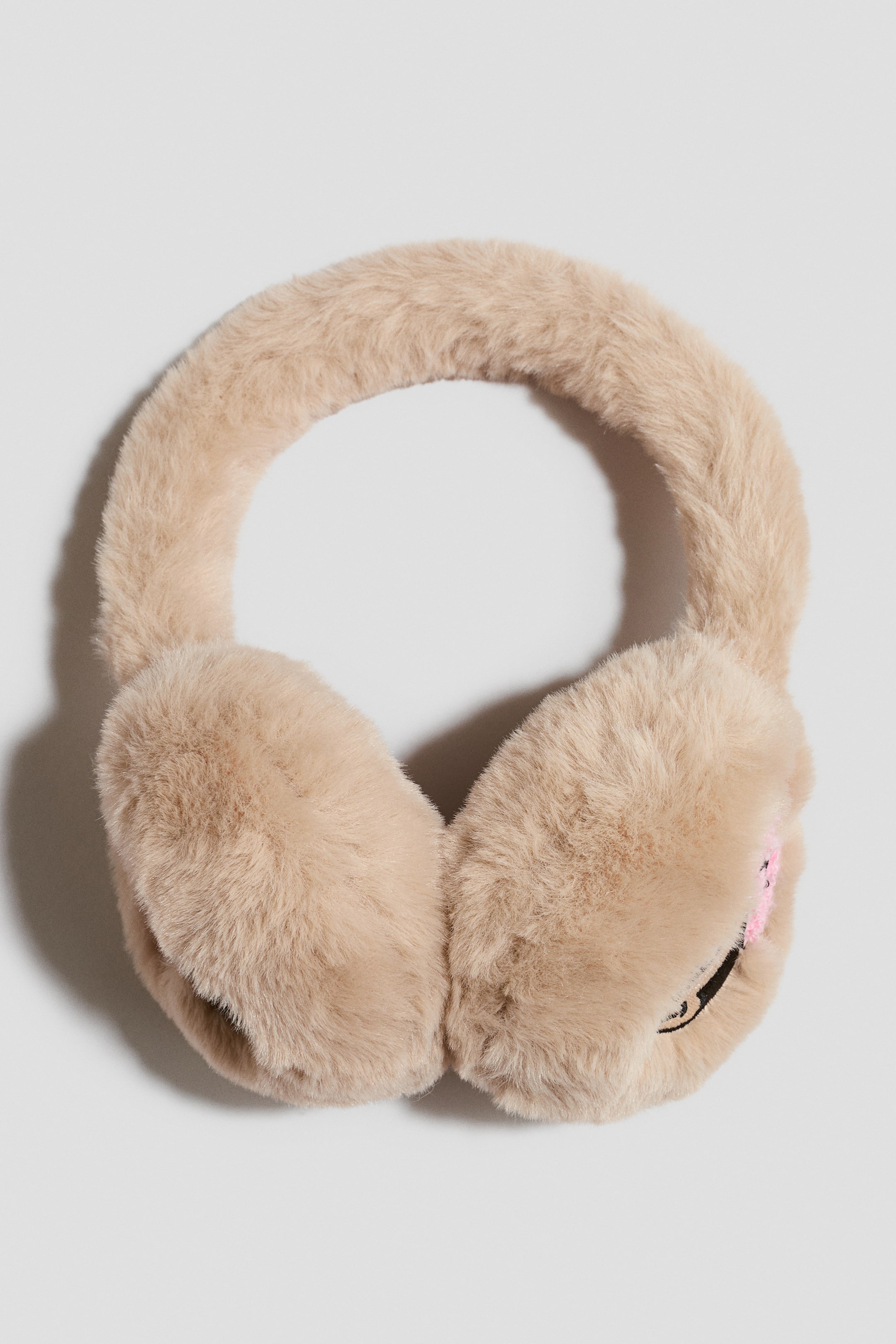 View larger image: Fluffy earmuffs are made of light brown faux fur, positioned at a slightly elevated front-facing angle. A small pink and black embroidered detail is visible on the outer side of the right ear cup.