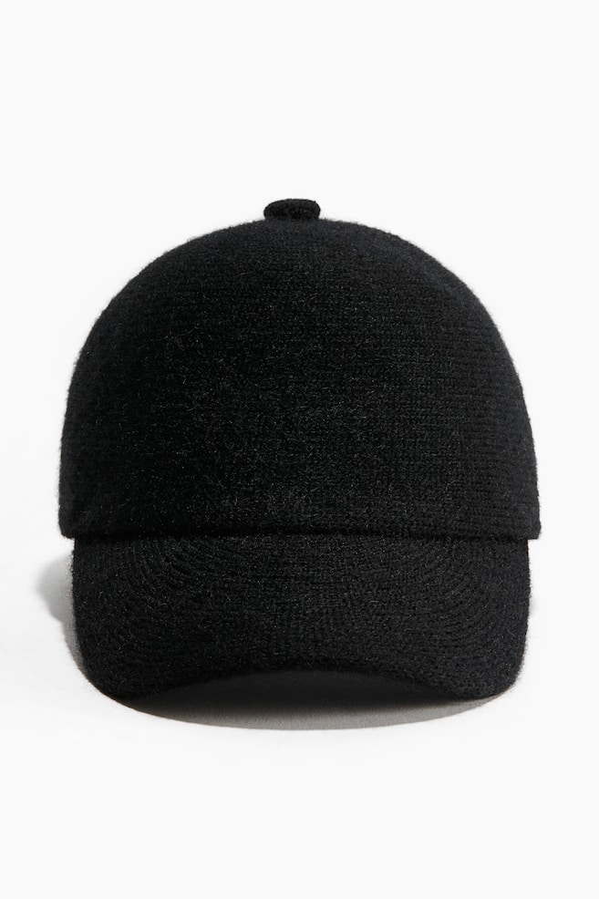 A black knit cap is shown from the front, featuring a soft, fuzzy texture and a structured, rounded crown. The cap is designed with a small matching button on the top and a curved peak. - 1