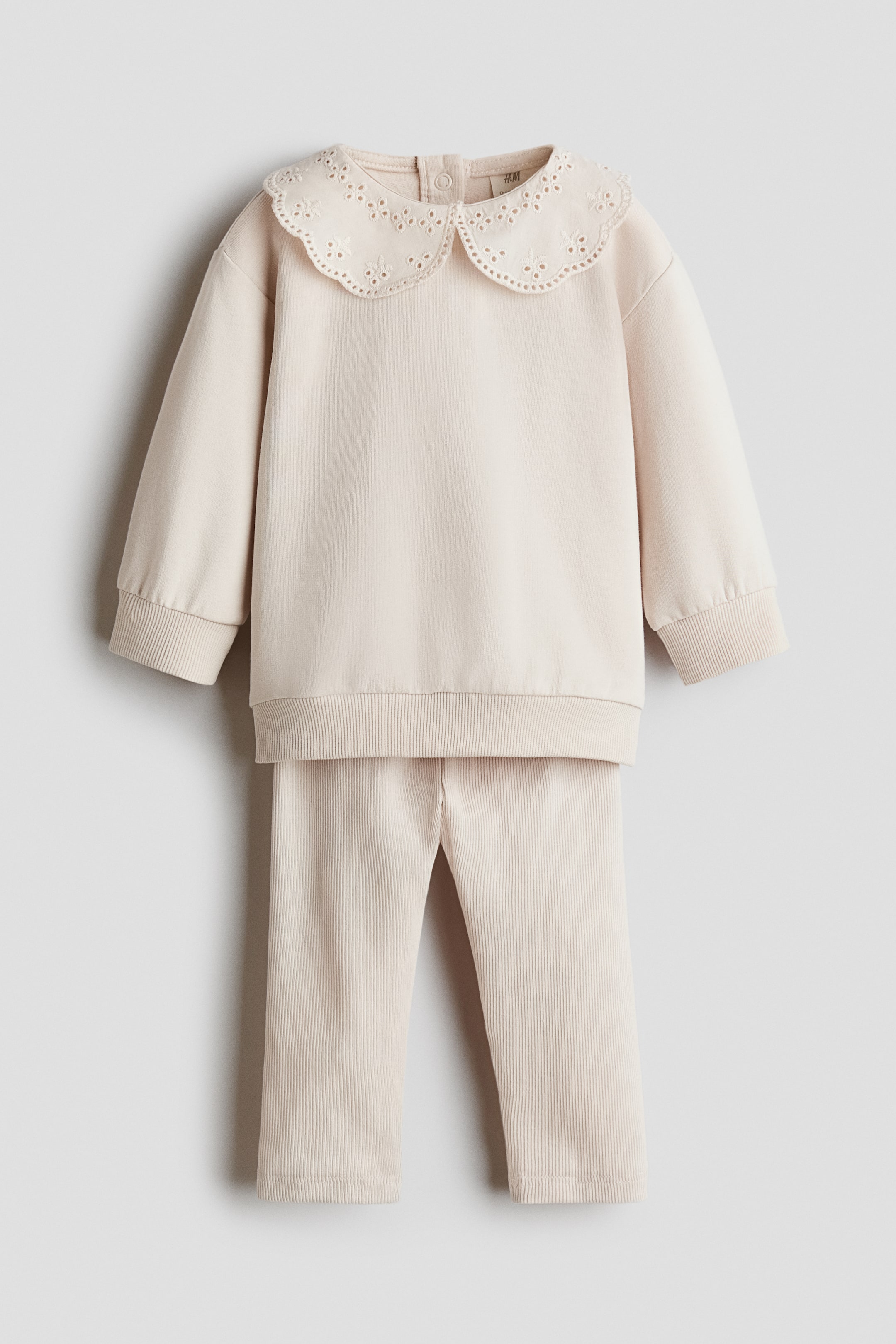 View larger image: A light beige two-piece baby set featuring a long-sleeved sweatshirt with an embroidered Peter Pan collar and ribbed cuffs and hem. The back of the neck features two small buttons. Matching ribbed trousers complete the set, with a straight-leg cut.