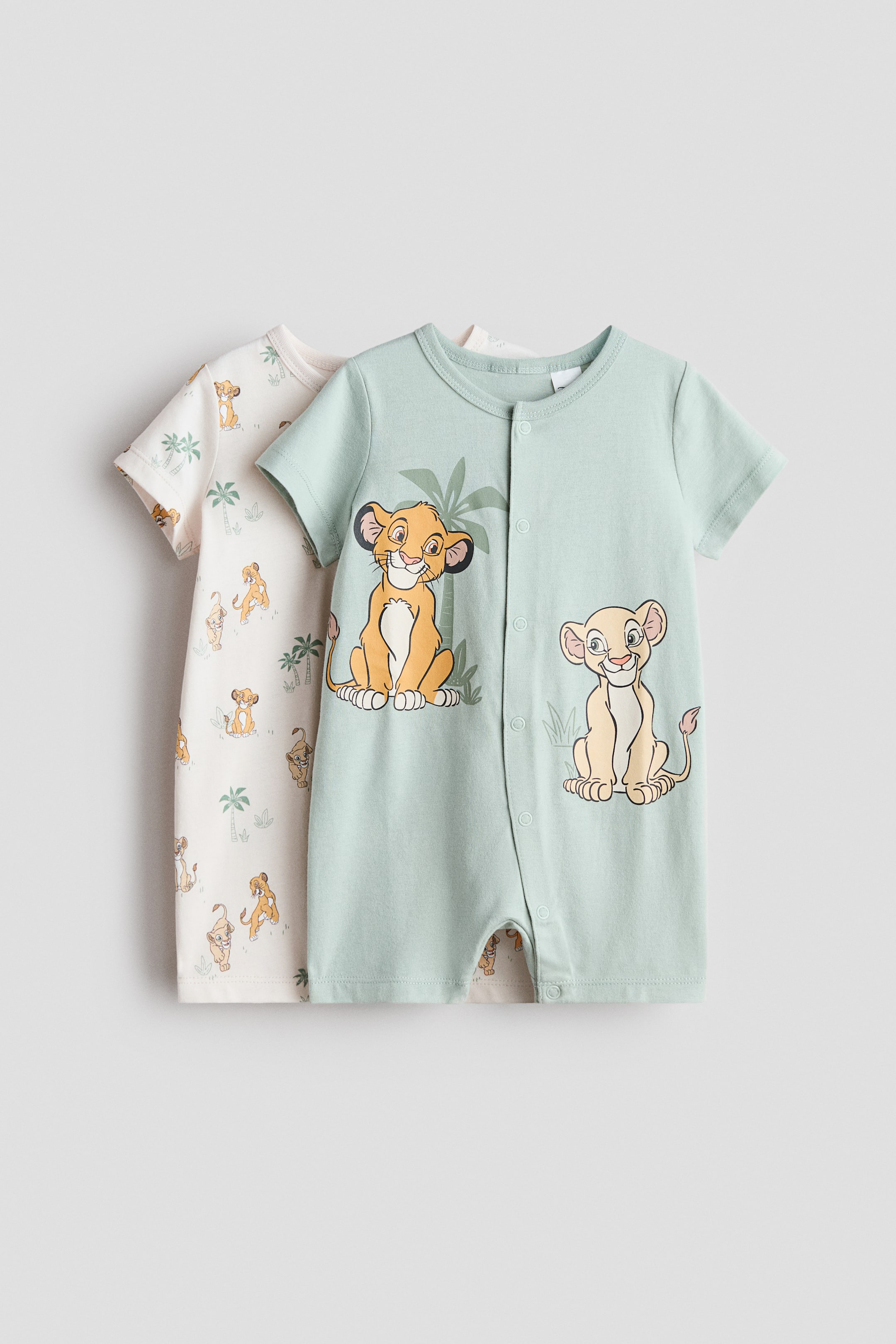查看大圖: 兩件短袖睡衣套裝，採用柔軟的印花棉質針織布製成，均為圓領設計，短褲款式。前面的睡衣是淺綠色，印有兩隻小獅子和棕櫚葉的大圖案，並配有豎排按鈕扣；而後面部分可見的睡衣則是米白色，印有小獅子和棕櫚樹的全版圖案。