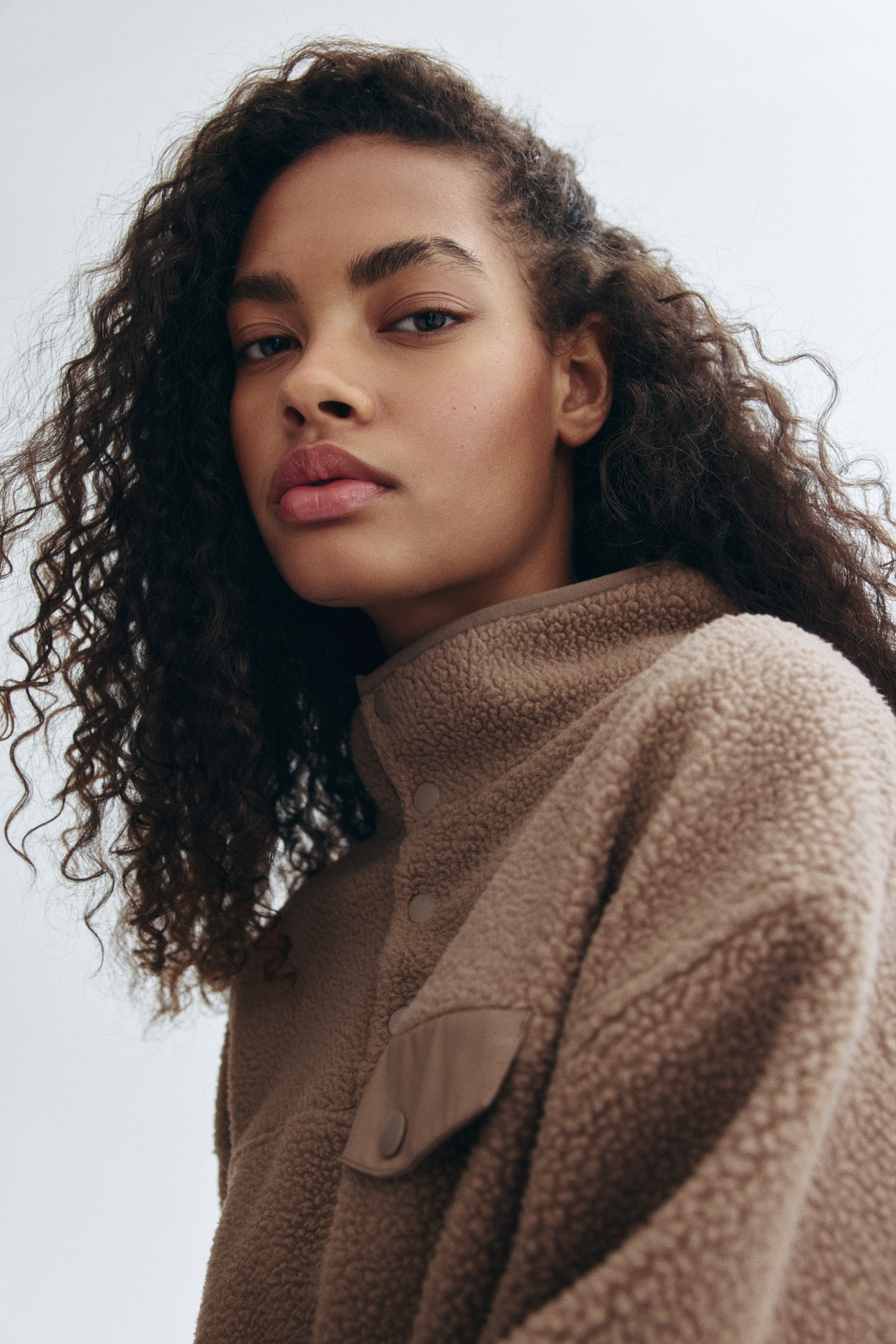 Agrandir l'image: Un pull polaire beige avec un col montant et une poche à rabat sur la poitrine fermée par un bouton-pression est porté par le mannequin.