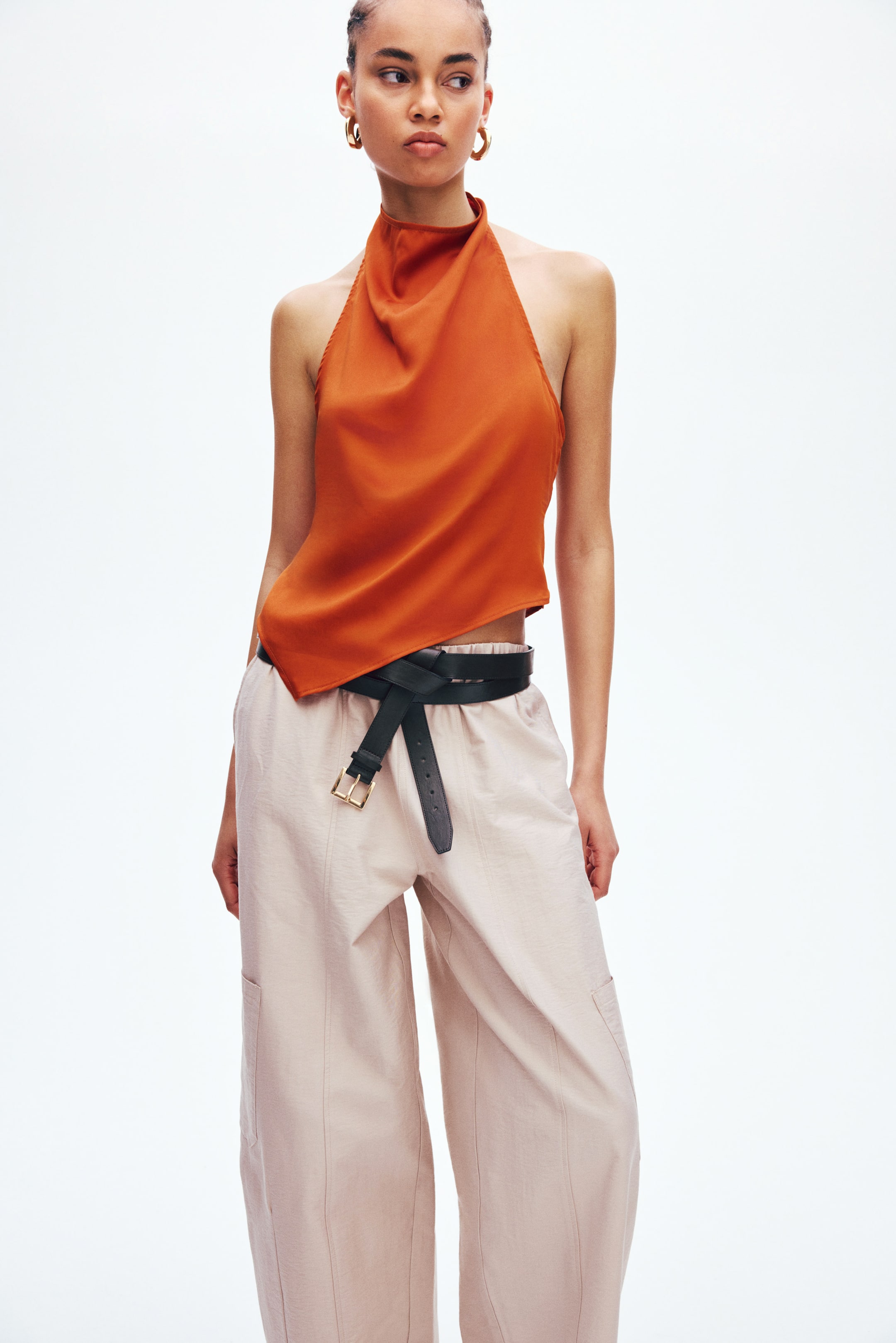 View larger image: Loose-fit trousers with a crisp weave, a high elasticated waist, diagonal side pockets, visible front seams, and patch pockets on their balloon legs are being worn by the model. A black belt is cinching the trousers at the waist.