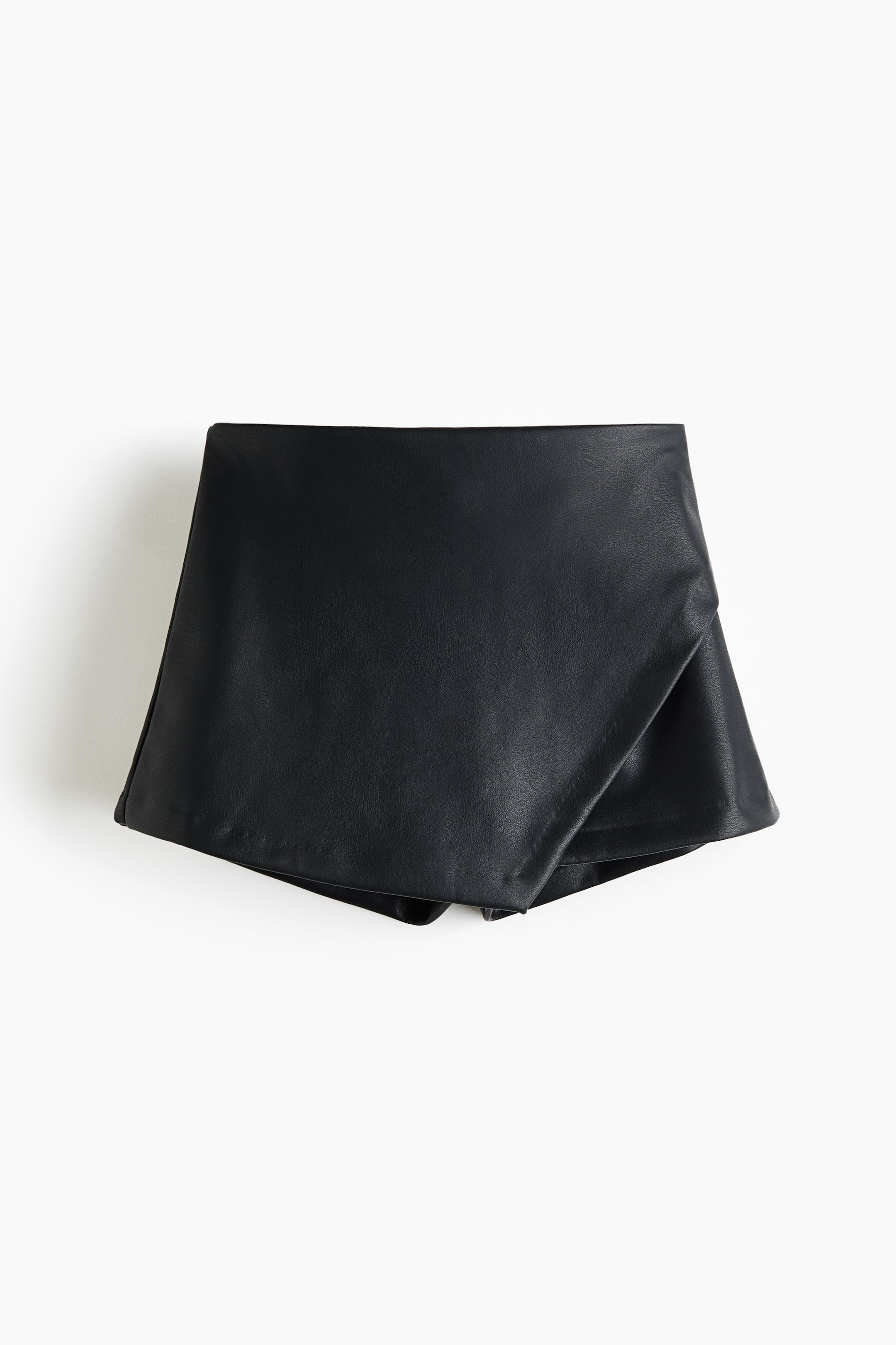 View larger image: Black faux leather skorts are laid flat, showcasing a smooth texture and a wide, flat waistband. An overlapping front panel gives it a skirt-like appearance.