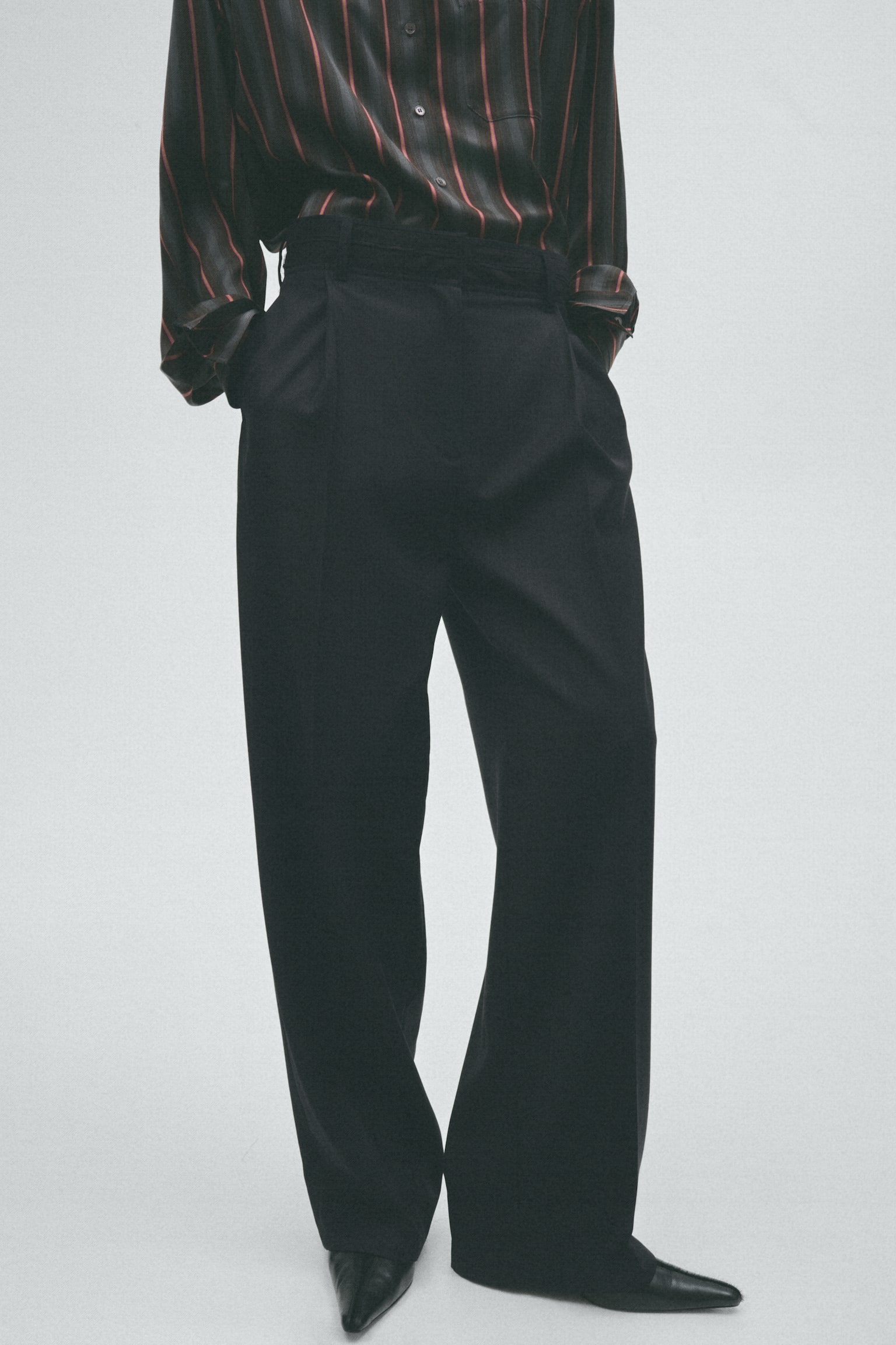 Black pinstriped trousers are showcased from the front, boasting a wide-leg cut, prominent front pleats, and a structured waistband with belt loops. - 1