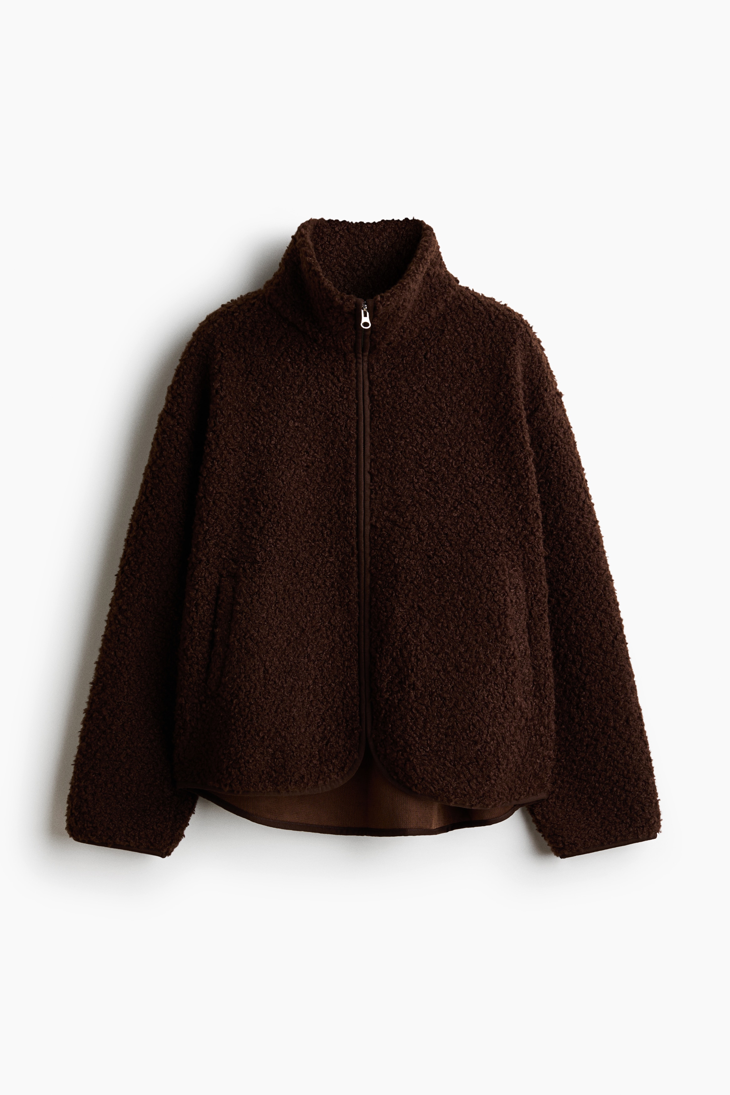 A dark brown teddy fleece jacket with a stand-up collar and front zipper is worn open by the model. The jacket is layered over a striped long-sleeve shirt and paired with wide-leg blue jeans.
